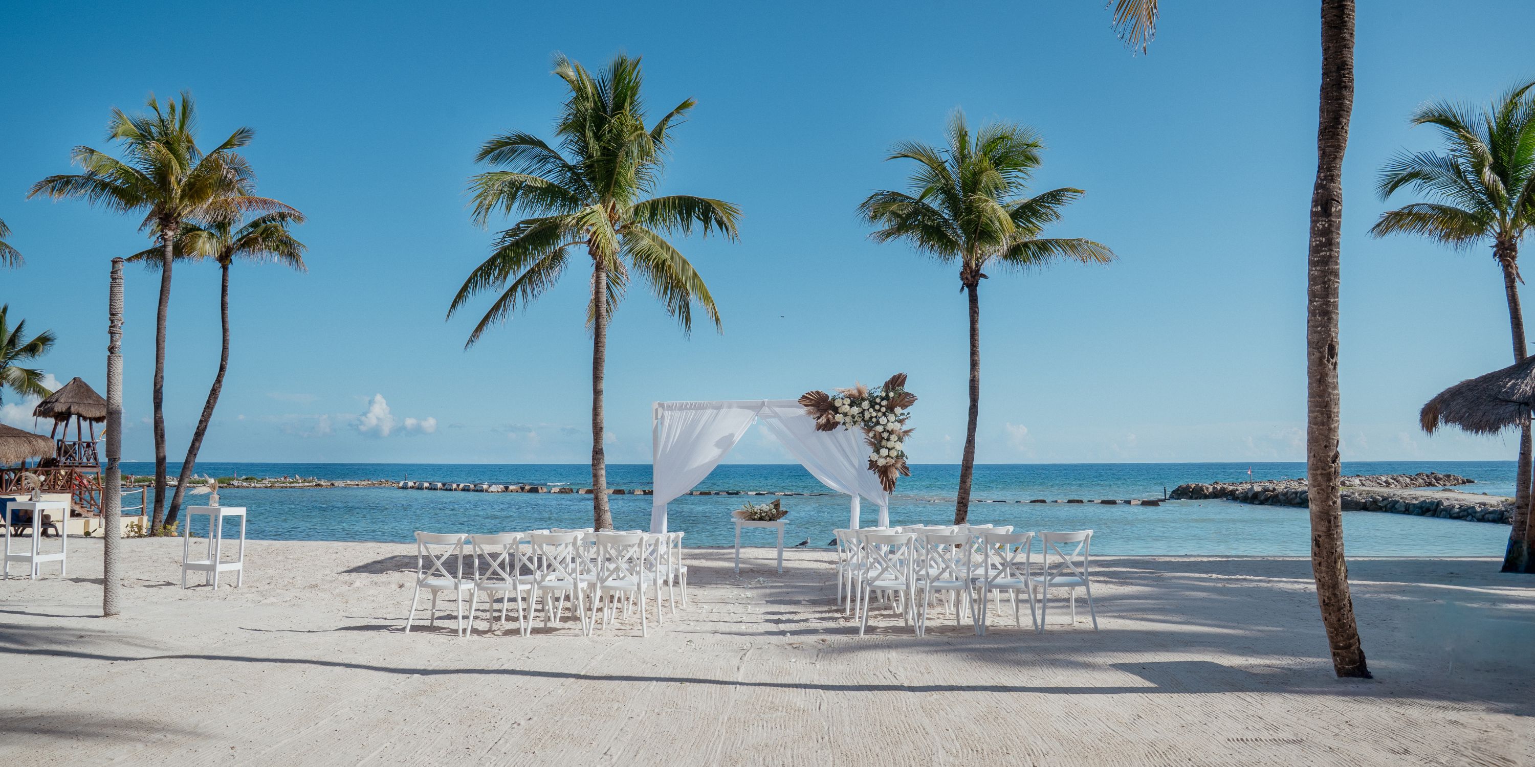 Destination wedding at Catalonia Riviera Maya: white chairs, canopy, palms, and ocean view on the beach.