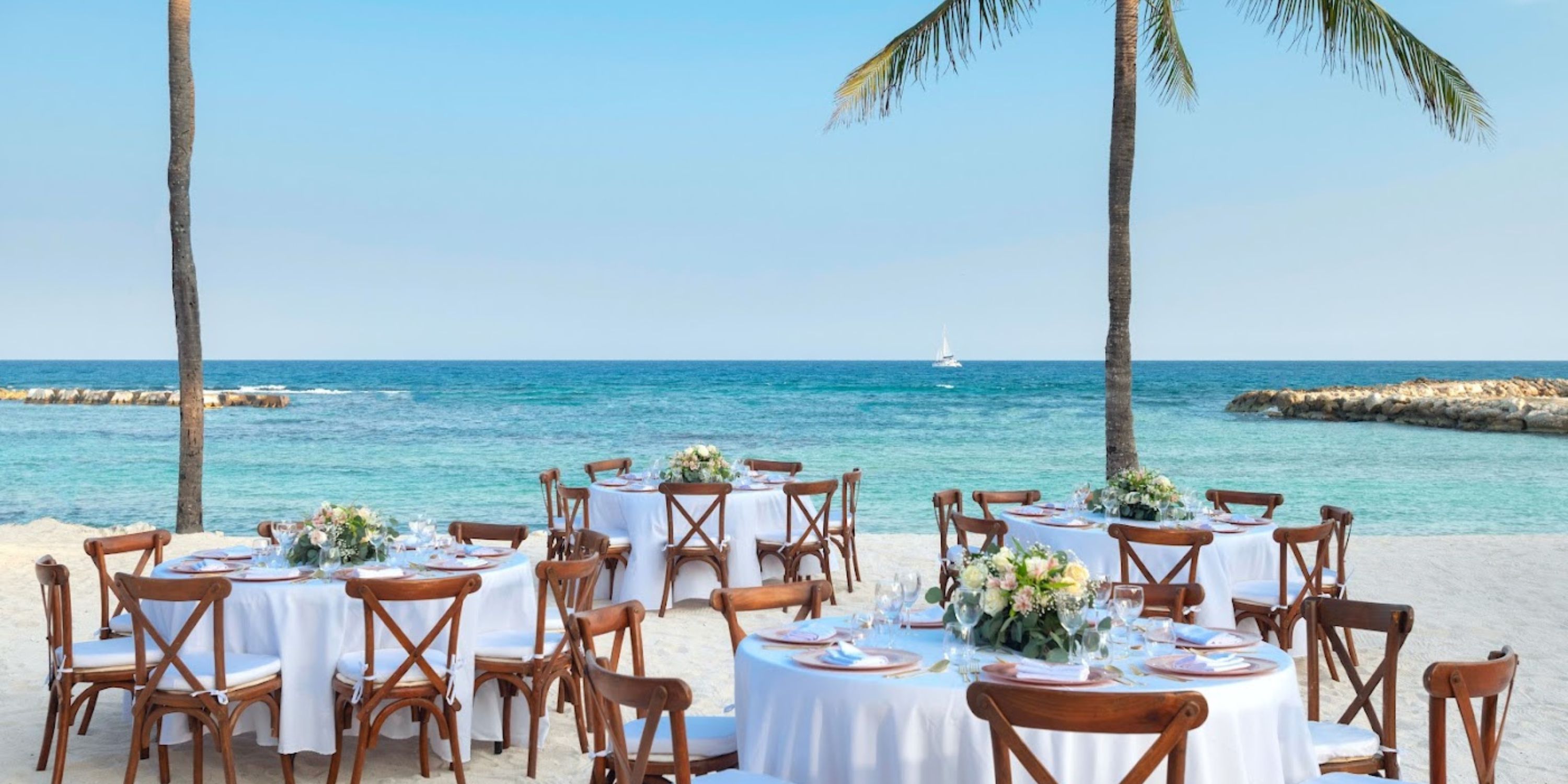 Round tables with floral centerpieces arranged for a destination wedding on the beach at Catalonia Riviera Maya.