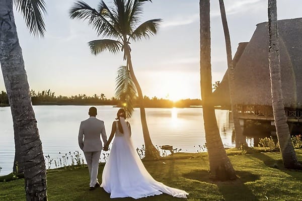 The bride and groom hold hands by the lake at sunset during their destination wedding at Occidental Cozumel.