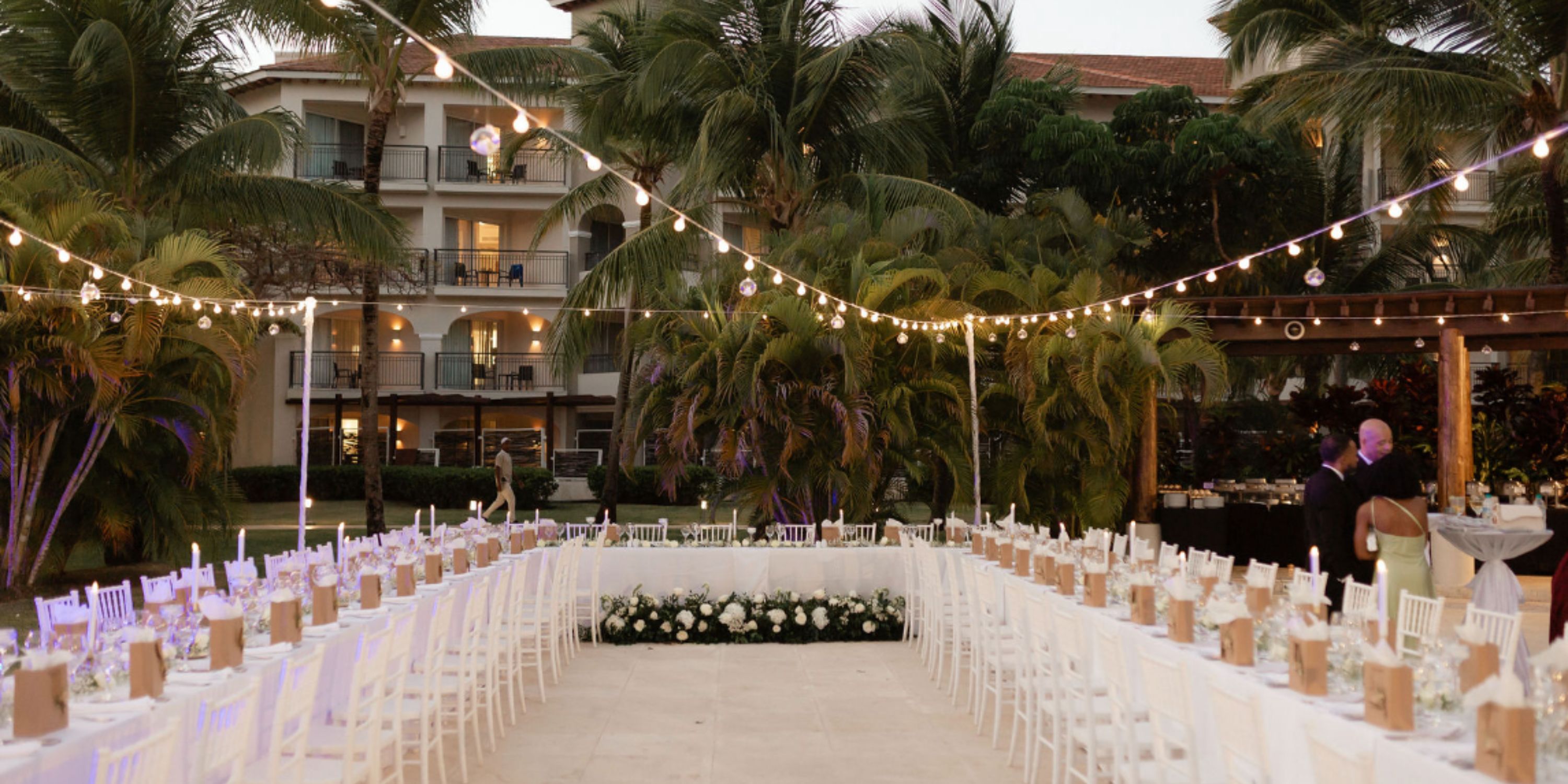 Destination wedding outdoor reception at Dreams Royal Beach Punta Cana with long tables, string lights, palms.