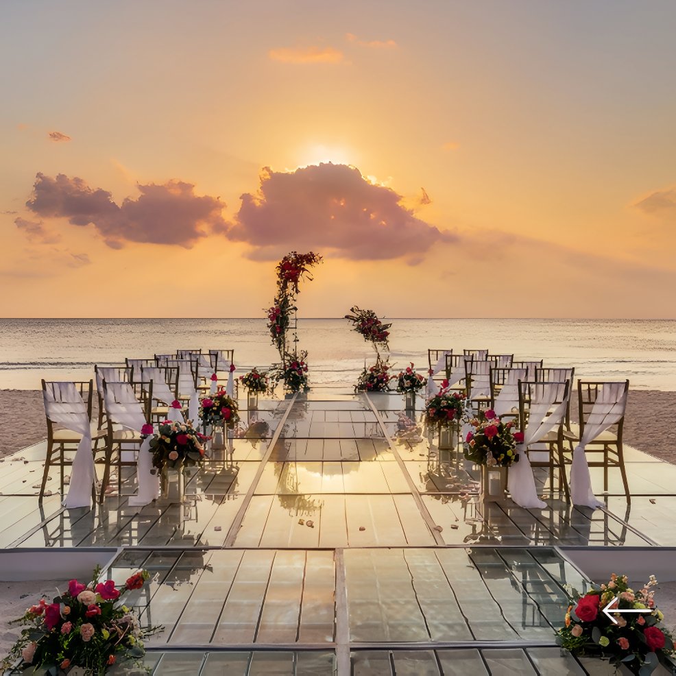 Destination wedding setup on the beach, featuring rows of chairs and floral decor as the sun sets.