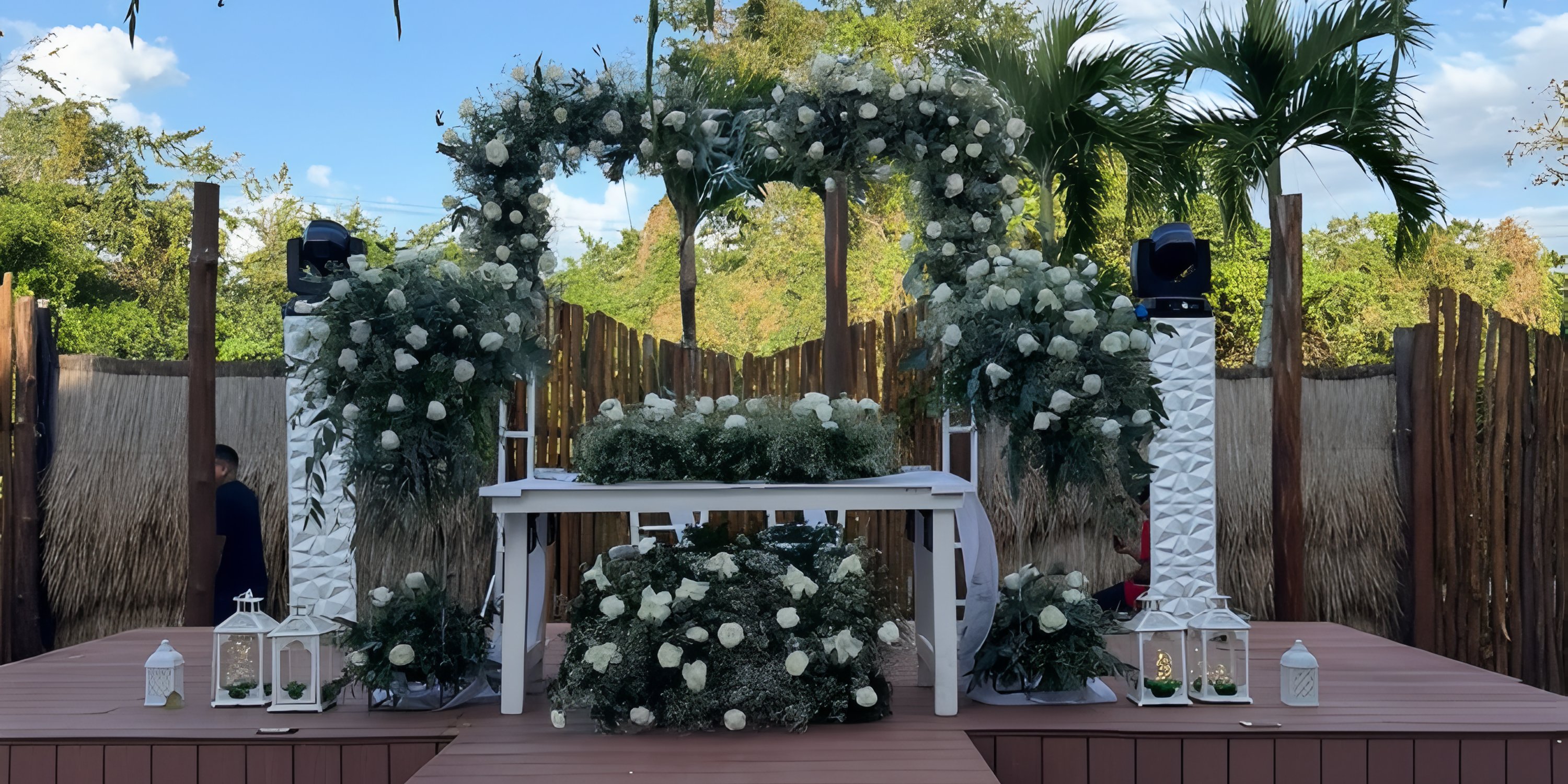 Wedding altar with white flowers, greenery, and lanterns on wooden stage at destination Dreams Cozumel Cape.