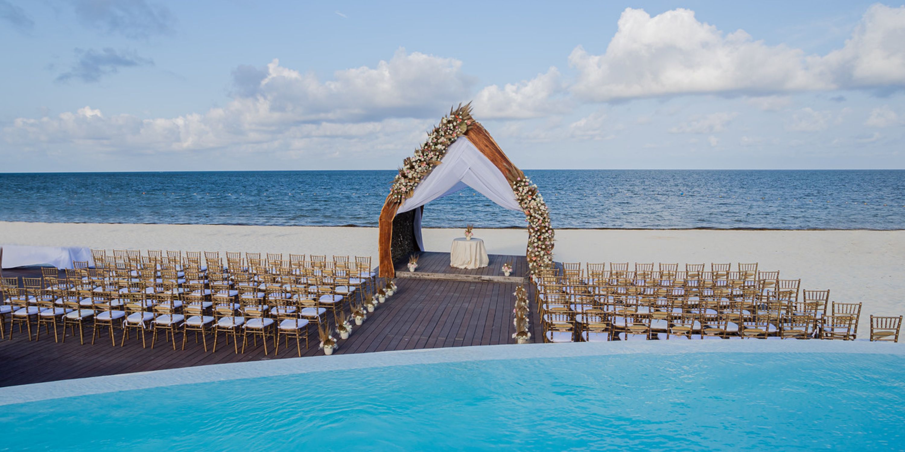 Rows of chairs face a wedding arch at Dreams Natura, with ocean and sky views for this destination wedding.