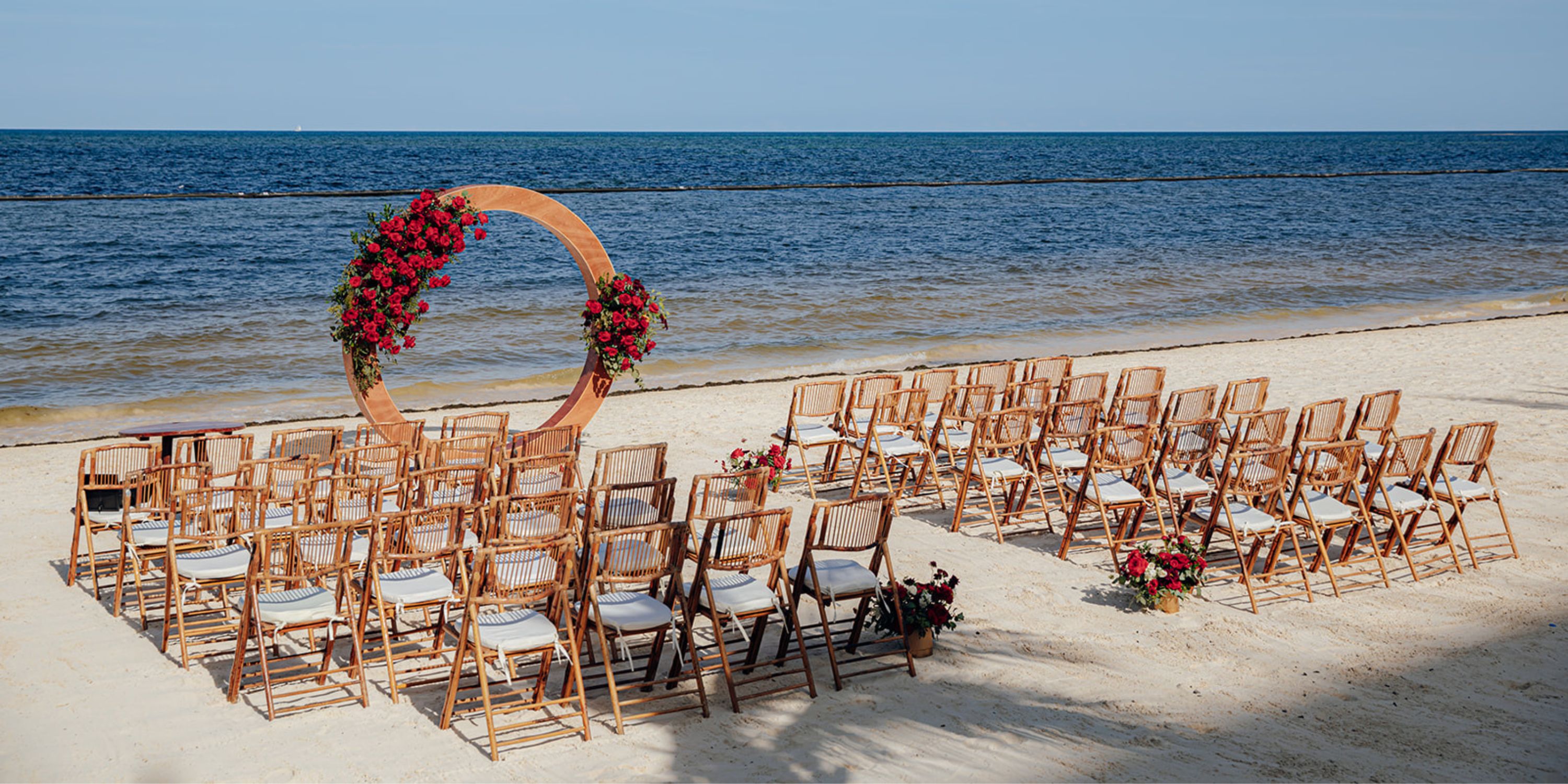 Rows of chairs face a circular floral arch on the beach at Dreams Natura for a destination wedding by the ocean.