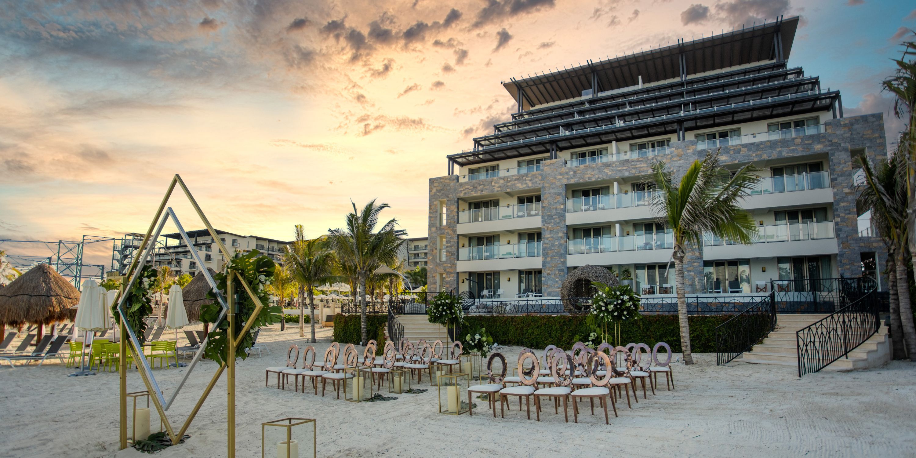Destination wedding ceremony on the beach at Dreams Natura, modern hotel in the sunset background.