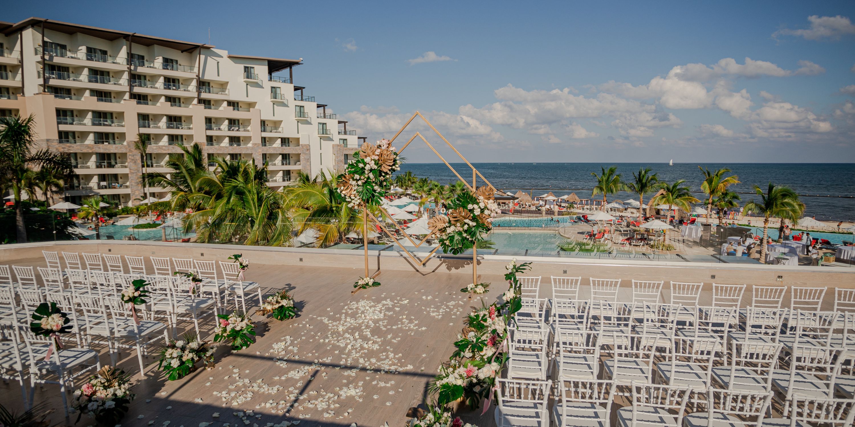 Destination wedding at Dreams Natura: oceanfront poolside setup with white chairs and floral decor.