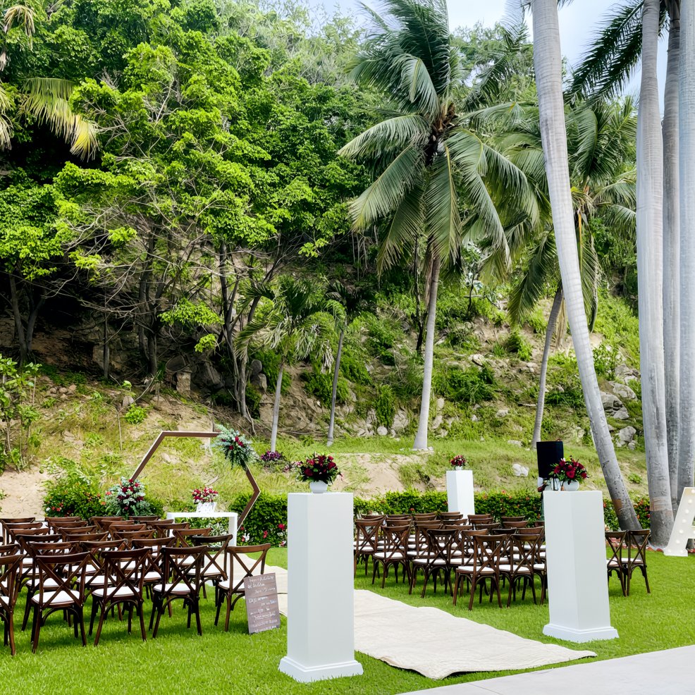 Destination wedding ceremony setup featuring rows of chairs, elegant floral displays, and palm trees behind.