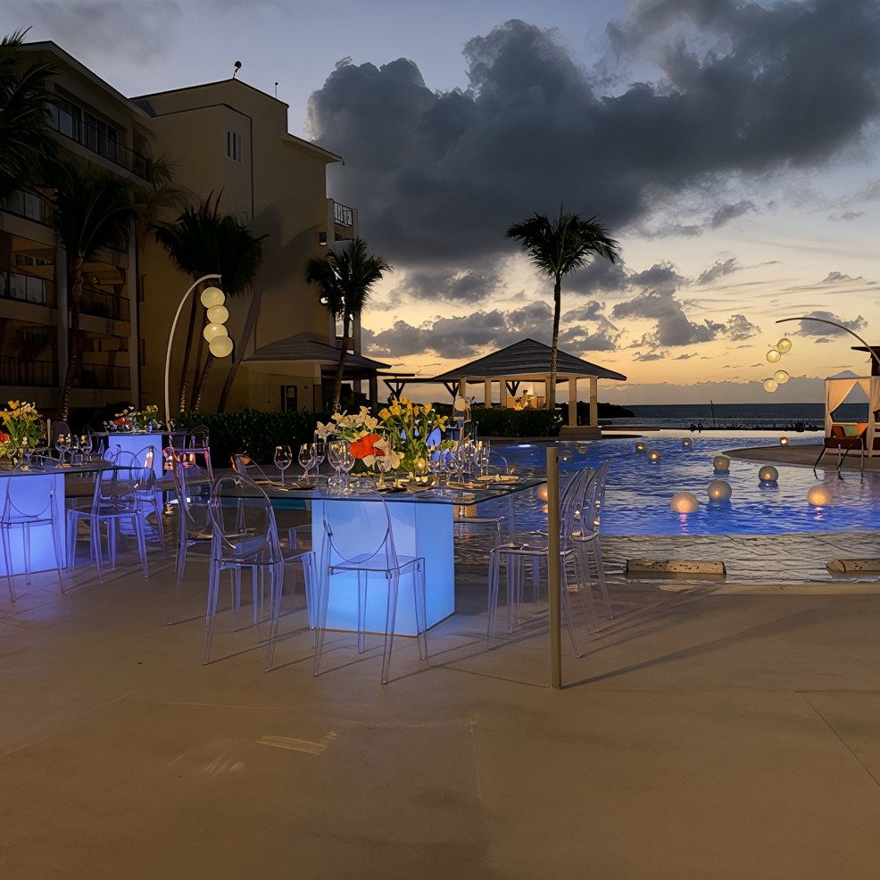 Poolside destination wedding dining with glowing tables at sunset, palm trees, and floral centerpieces.