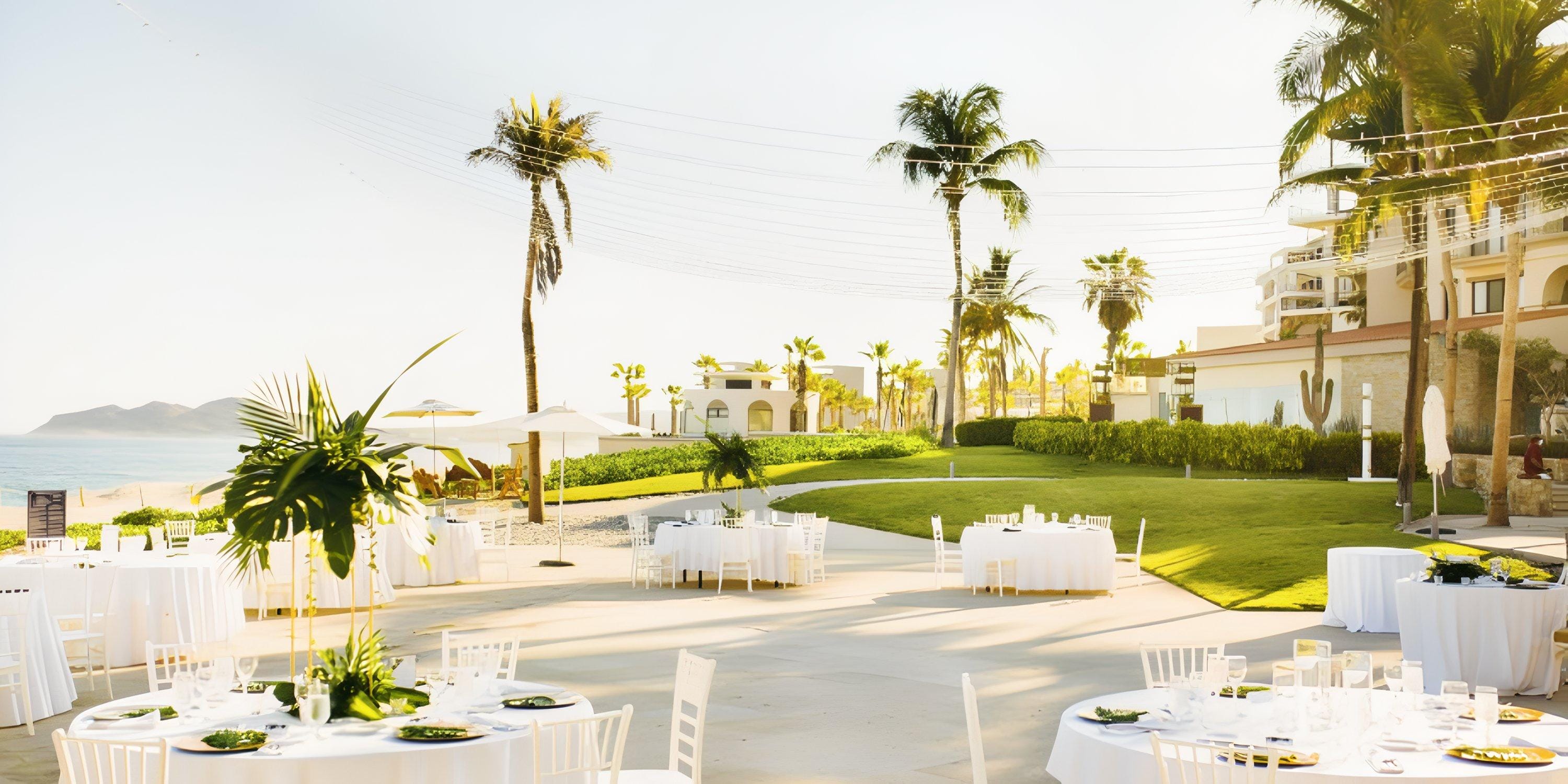 Destination wedding setup at Dreams Los Cabos with round tables, white chairs, palms, and string lights.