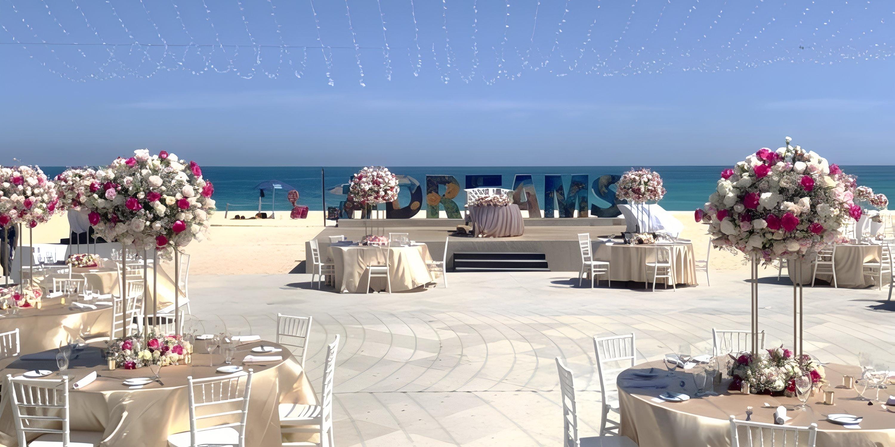 Destination wedding setup at Dreams Los Cabos with round tables, flowers, and a large "DREAMS" sign.