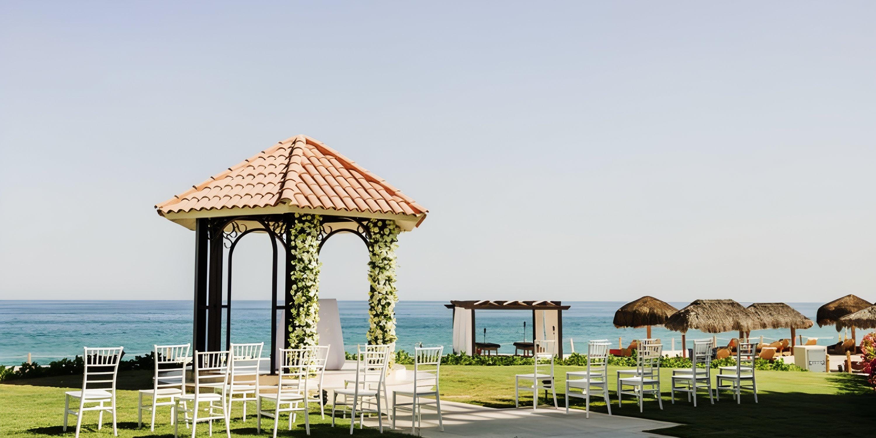 Dreams Los Cabos destination wedding: oceanfront setup featuring white chairs and a gazebo with flowers.