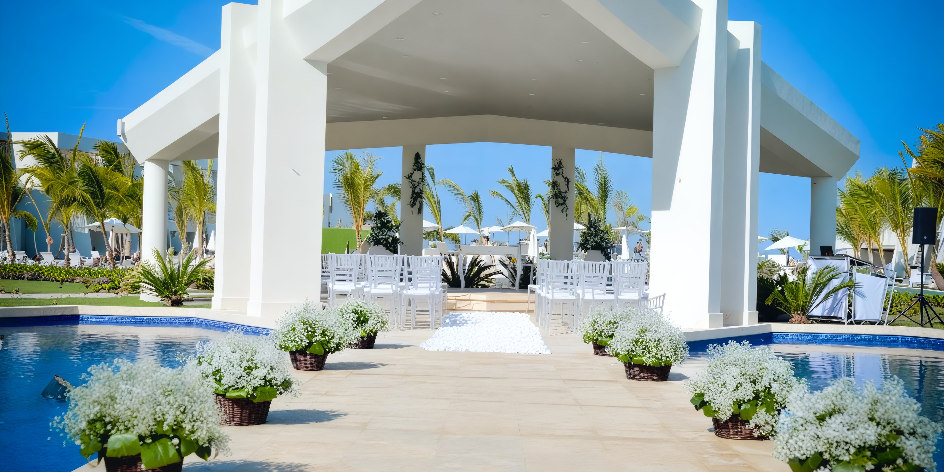 Dreams Onyx venue offers an idyllic setting for destination weddings, featuring elegant white chairs, stunning floral decor, and a picturesque poolside view perfect for outdoor ceremonies.