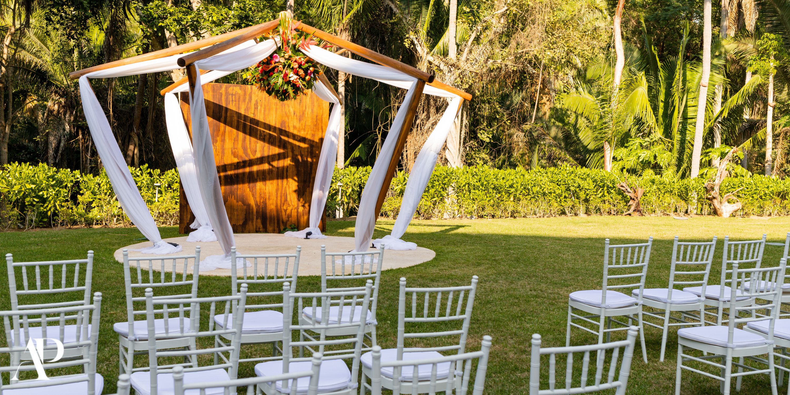 Dreams Bahia Mita destination wedding altar with white drapes, lawn chairs, and lush greenery.
