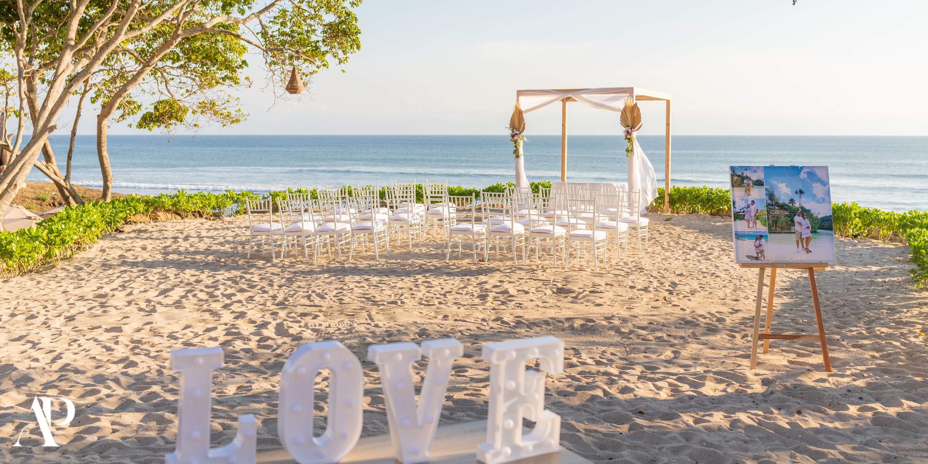 Destination wedding setup at Dreams Bahia Mita beach with white chairs, floral arch, and LOVE sign in sand.