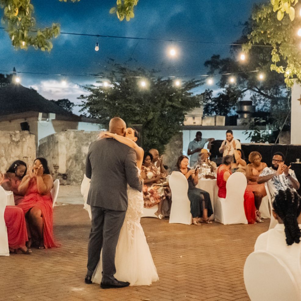 At a destination wedding, the bride and groom dance outdoors while guests watch and capture photos.