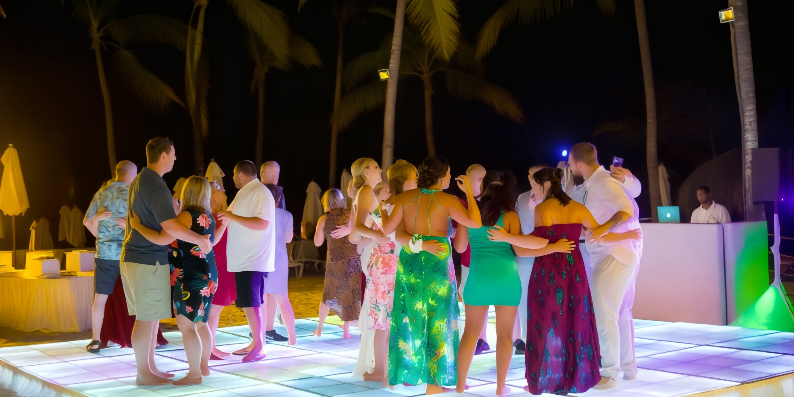 Dreams Dominicus: Guests celebrating a destination wedding dance on an illuminated floor at night, surrounded by the gentle sway of palm trees.