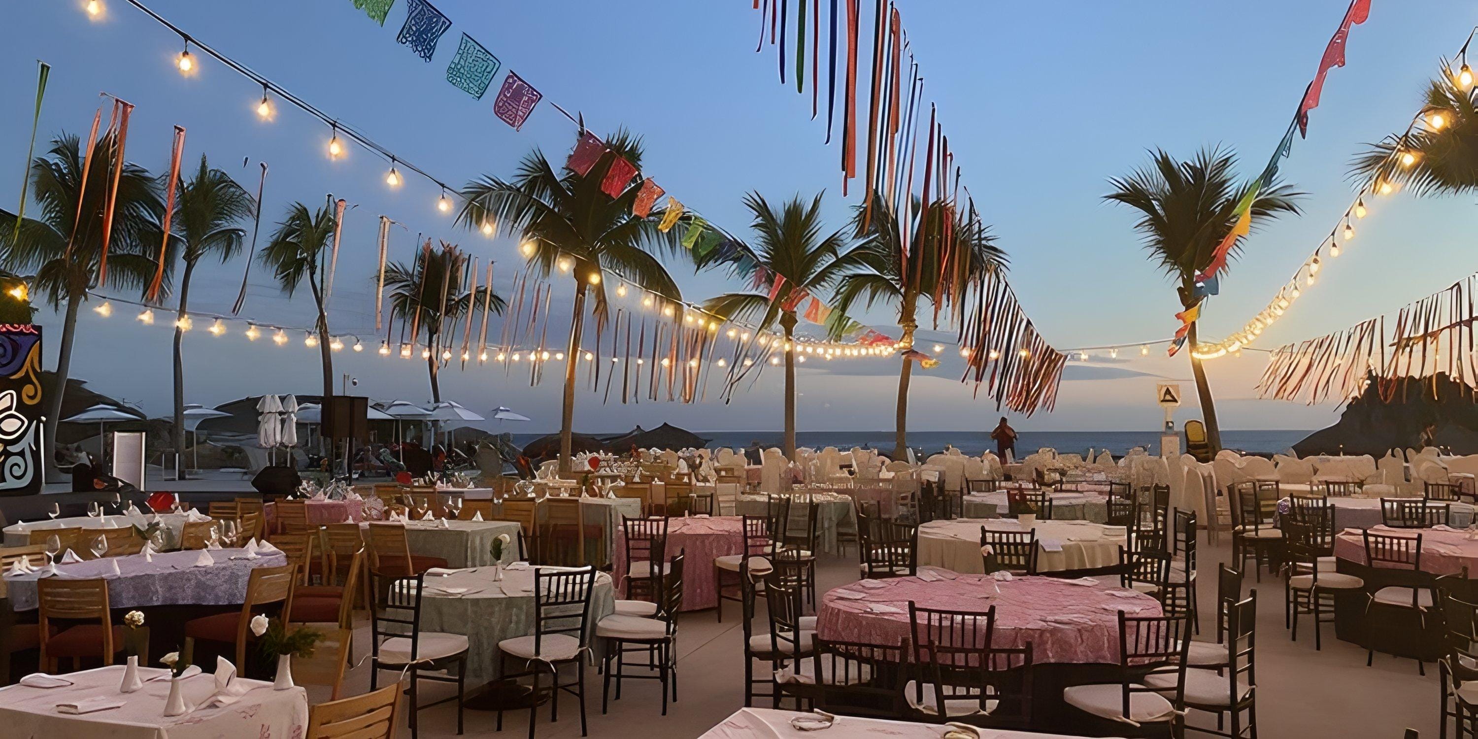 Dreams Huatulco: destination wedding tables by the sea at sunset, with string lights and palm trees.