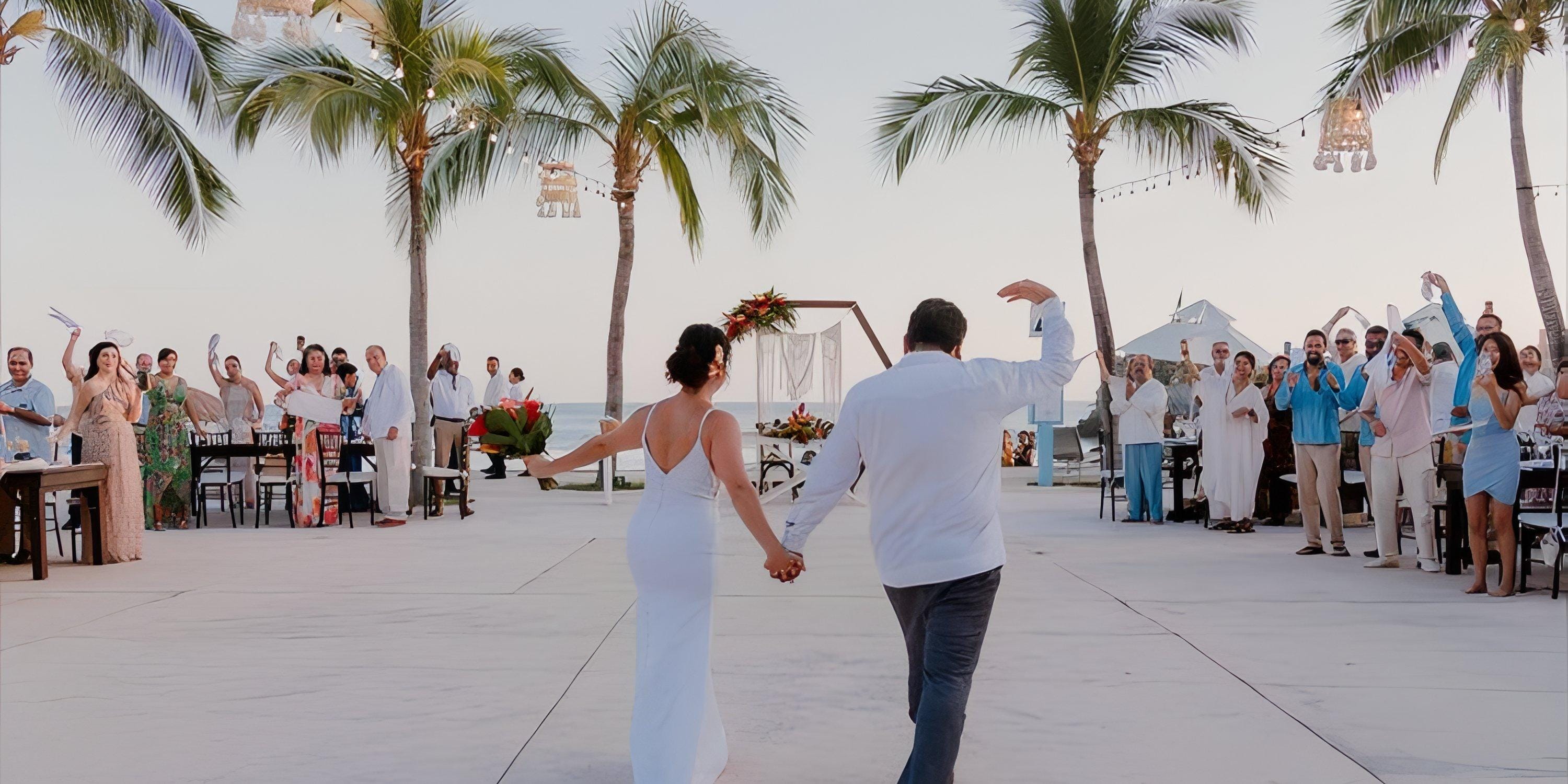 A bride and groom walk hand in hand at their Dreams Huatulco destination wedding reception outdoors.