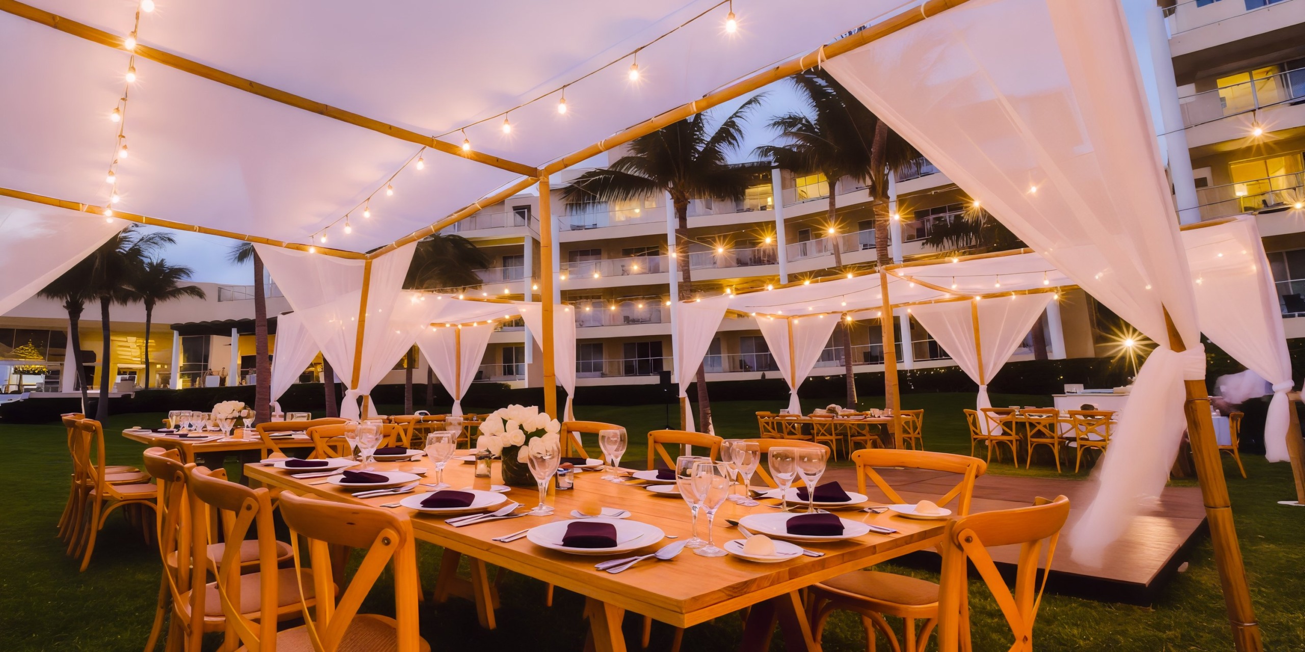 The outdoor area at Dreams Jade Riviera Cancun is beautifully adorned with wooden tables and chairs, complemented by string lights and a white canopy, creating the perfect setting for a destination wedding.
