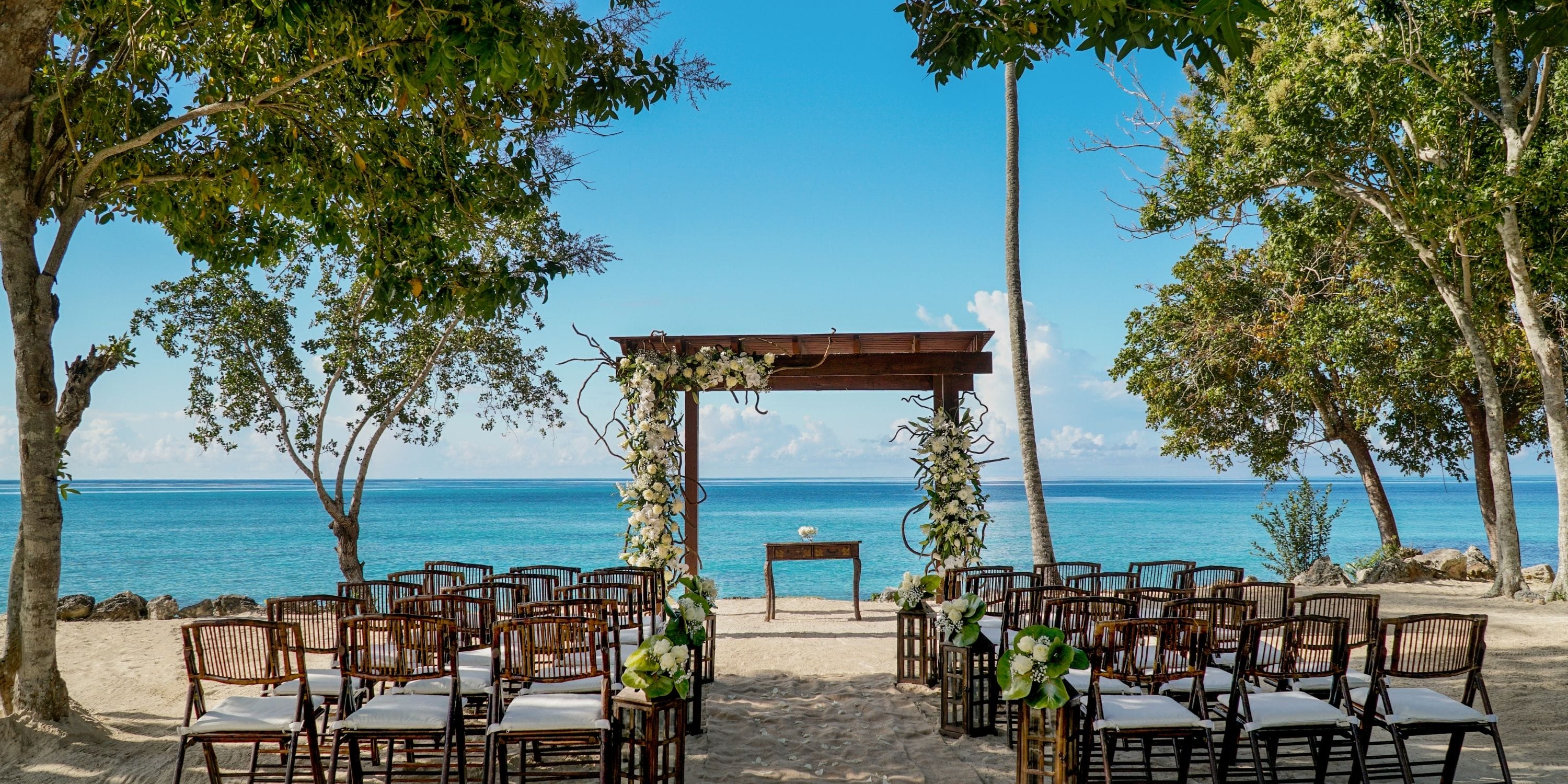 Chairs and a floral arch arranged on the beach for a destination wedding at Dreams La Romana.