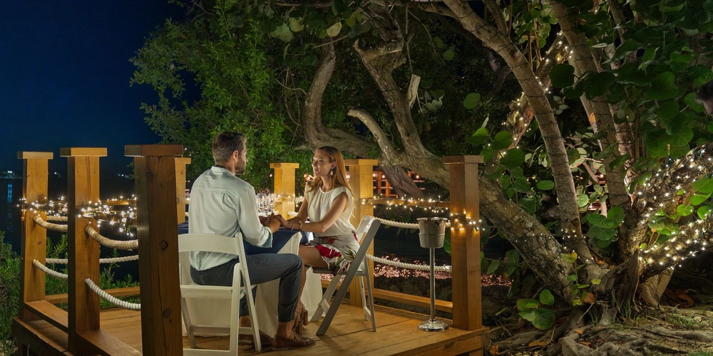 A couple enjoys an intimate outdoor dinner at Hilton La Romana, basking in the glow of string lights and trees under the night sky—an enchanting setting perfect for a destination wedding.