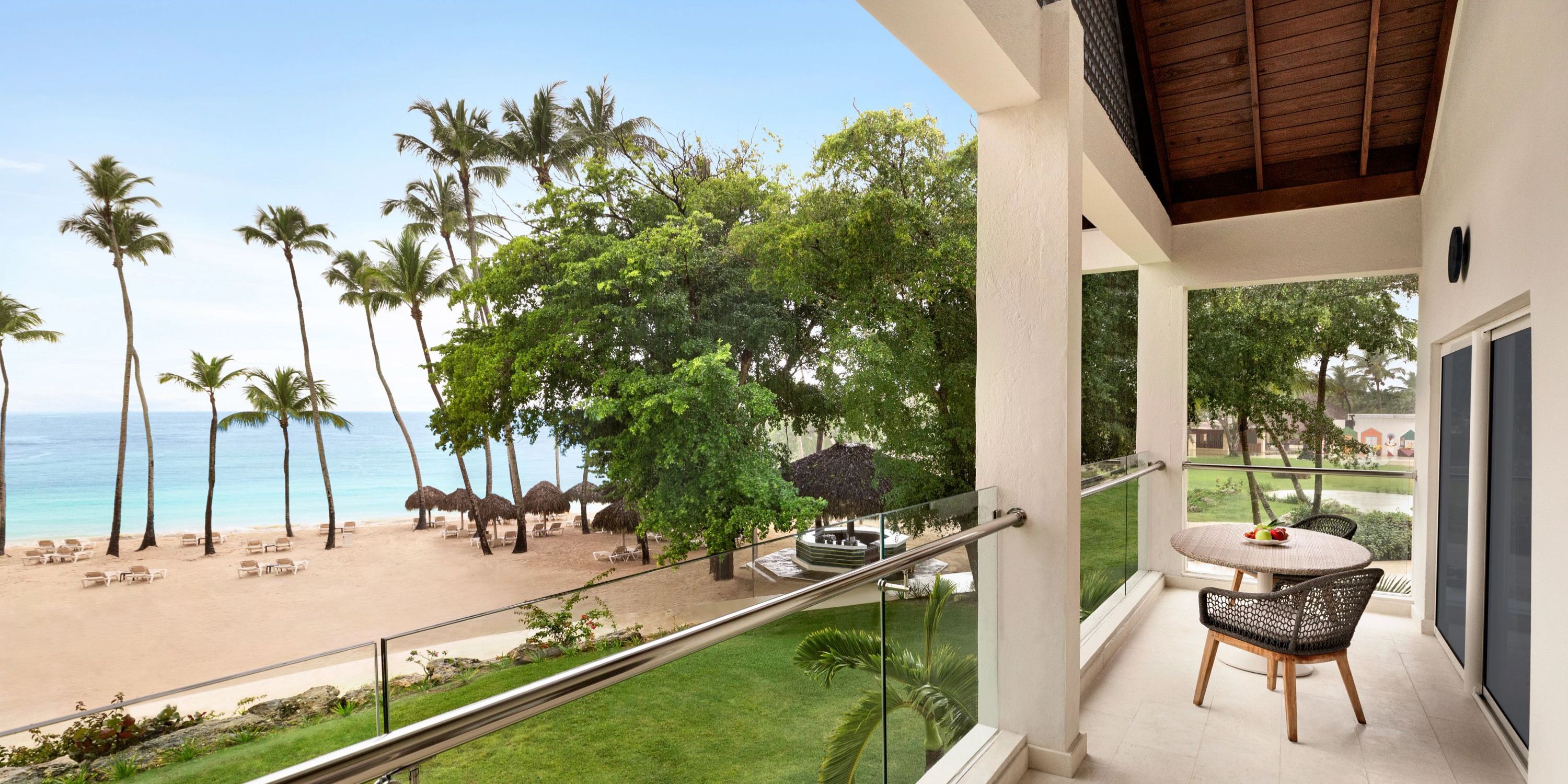 Hilton La Romana balcony featuring a table and chairs, offering stunning views of the sandy beach, swaying palms, and turquoise ocean—a perfect setting for a romantic destination wedding.