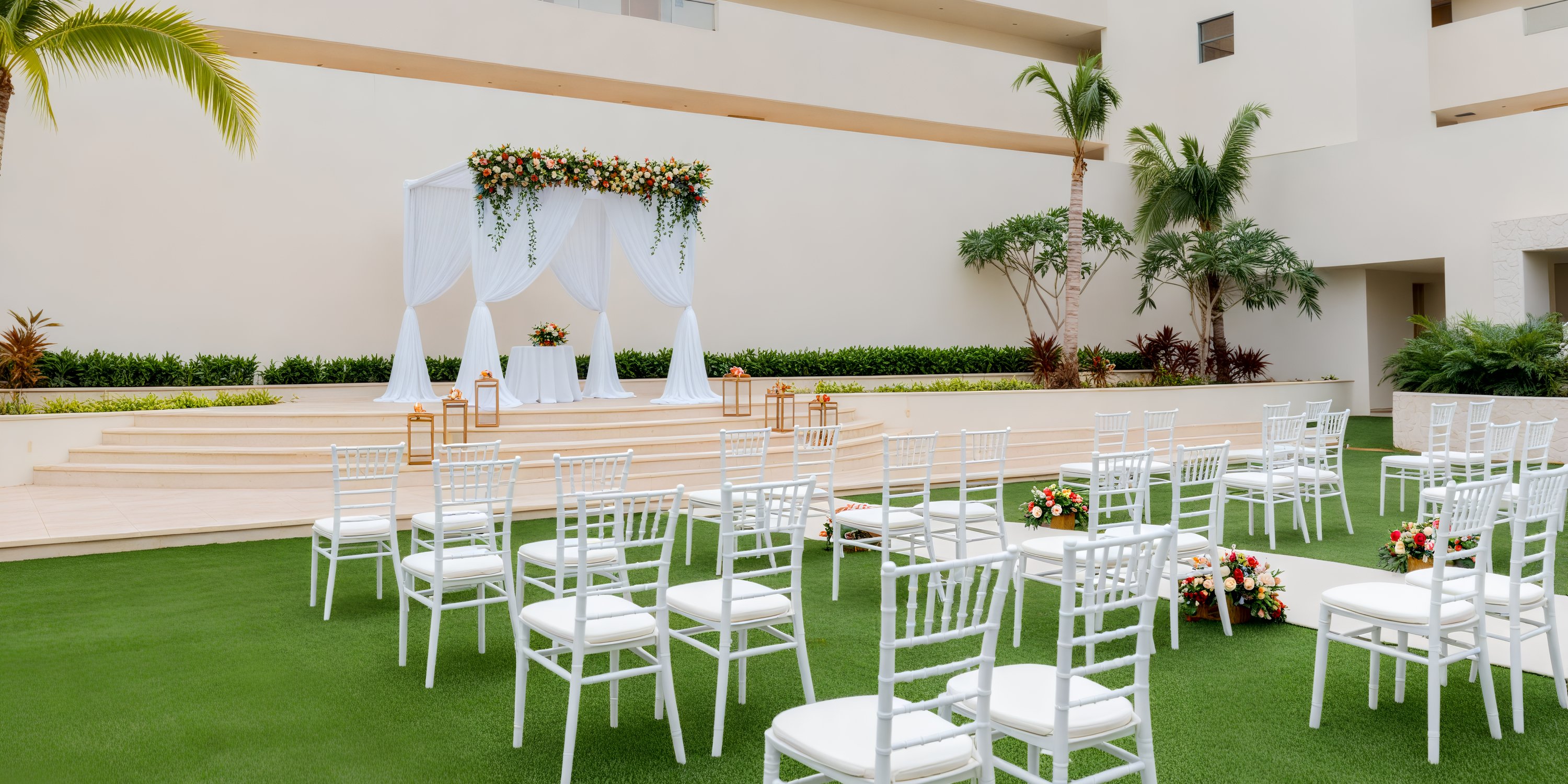 A dreamy destination wedding setup at Dreams Natura, featuring elegant white chairs and a beautifully adorned floral altar on a lush green lawn.