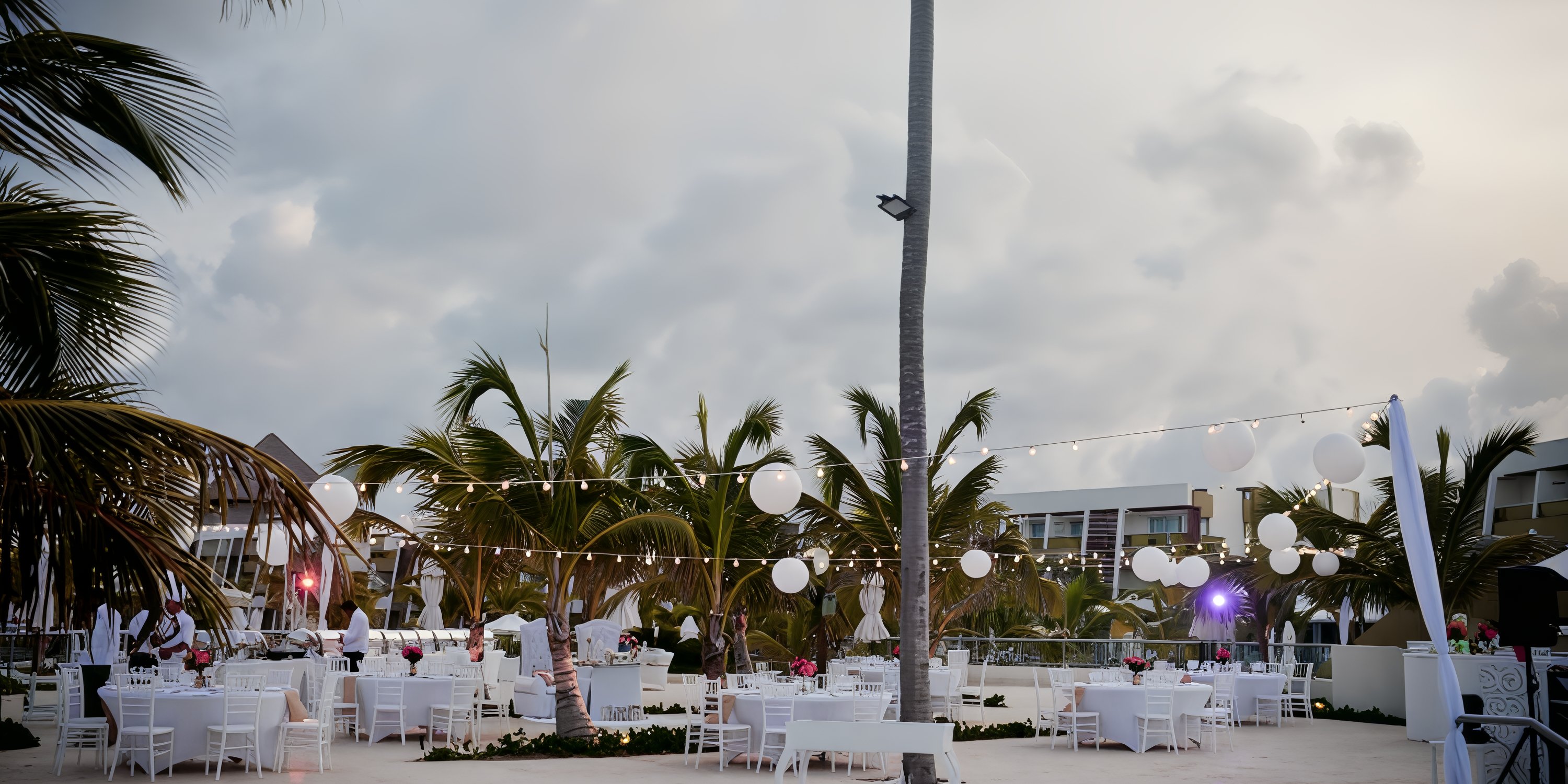 Dreams Onyx destination wedding setup with white tables, chairs, string lights, and palm trees at dusk.