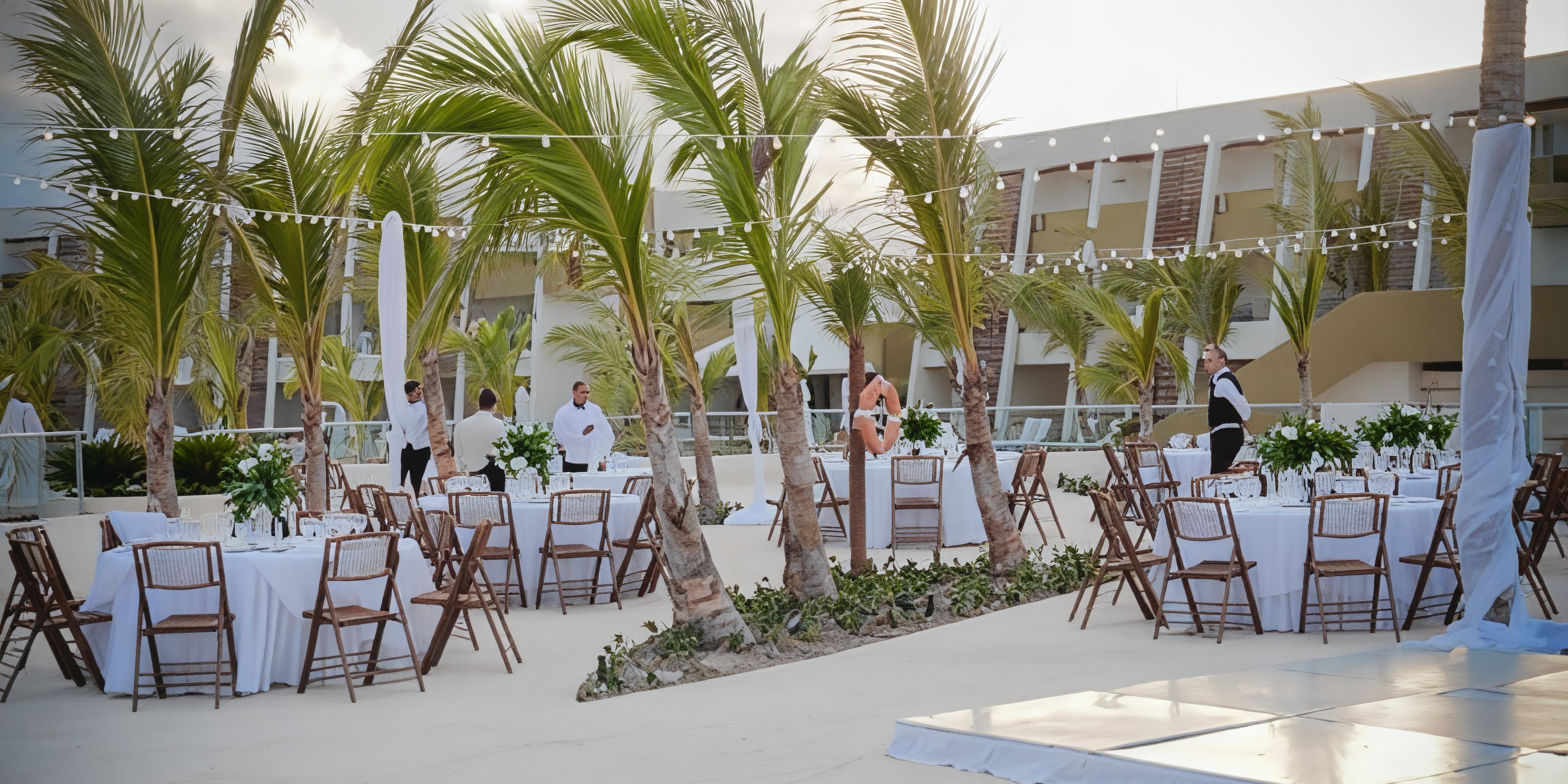 Dreams Onyx destination wedding setup with round tables, chairs, and string lights under palm trees.