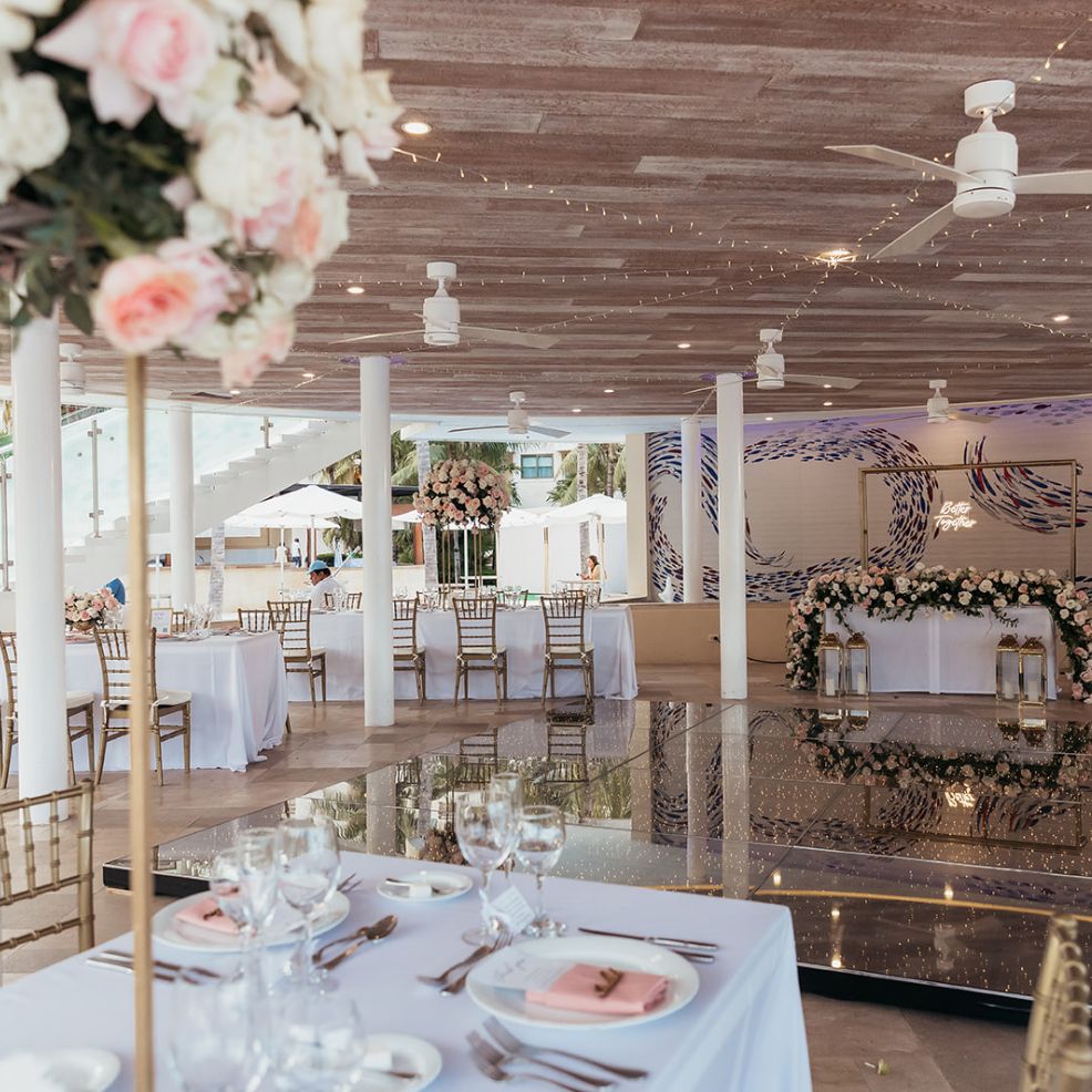Chic destination wedding reception featuring white tablecloths, gold chairs, and floral centerpieces.