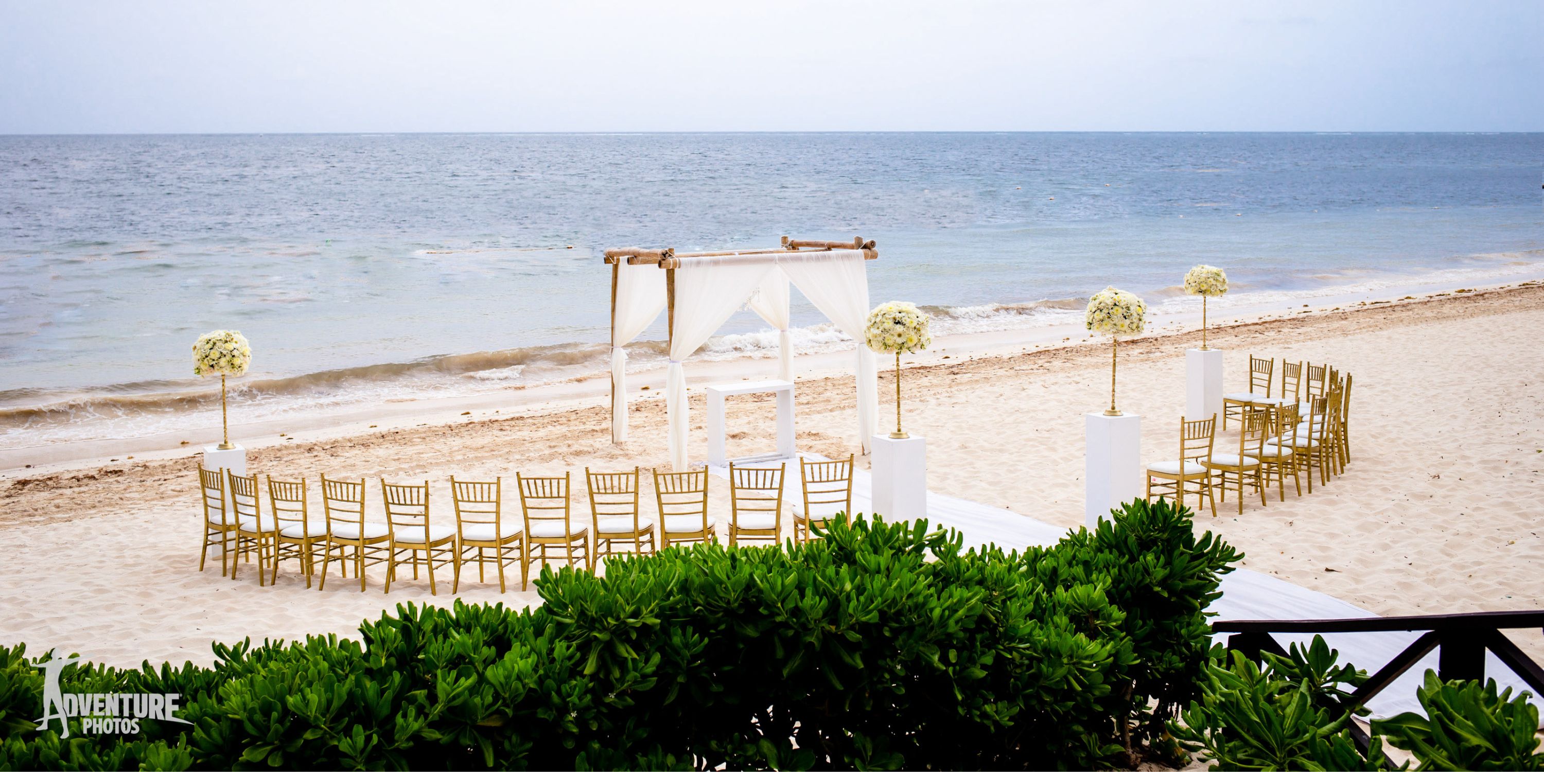 Destination wedding at Dreams Sapphire: gold chairs, floral decorations, and an arch by the ocean.