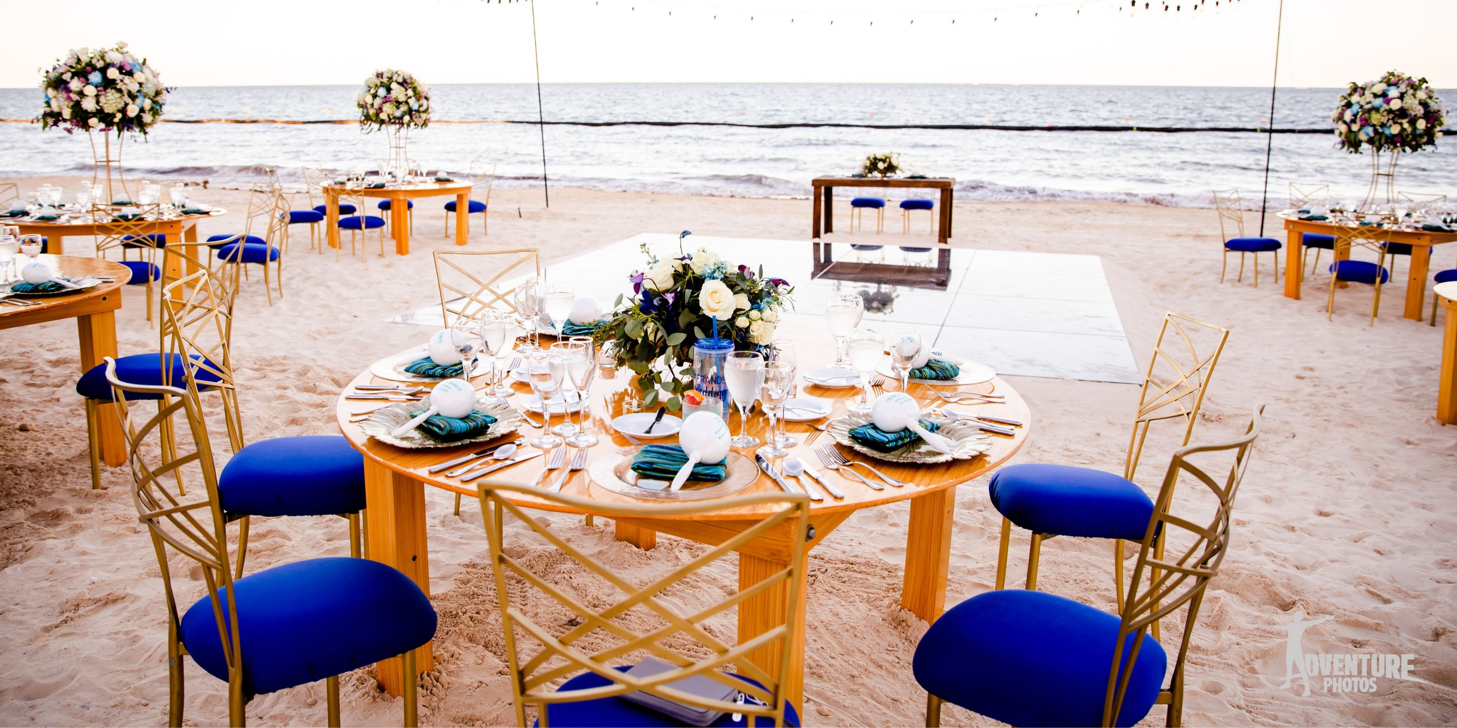 Dreams Sapphire: Round tables with blue chairs set up for a destination wedding by the ocean.