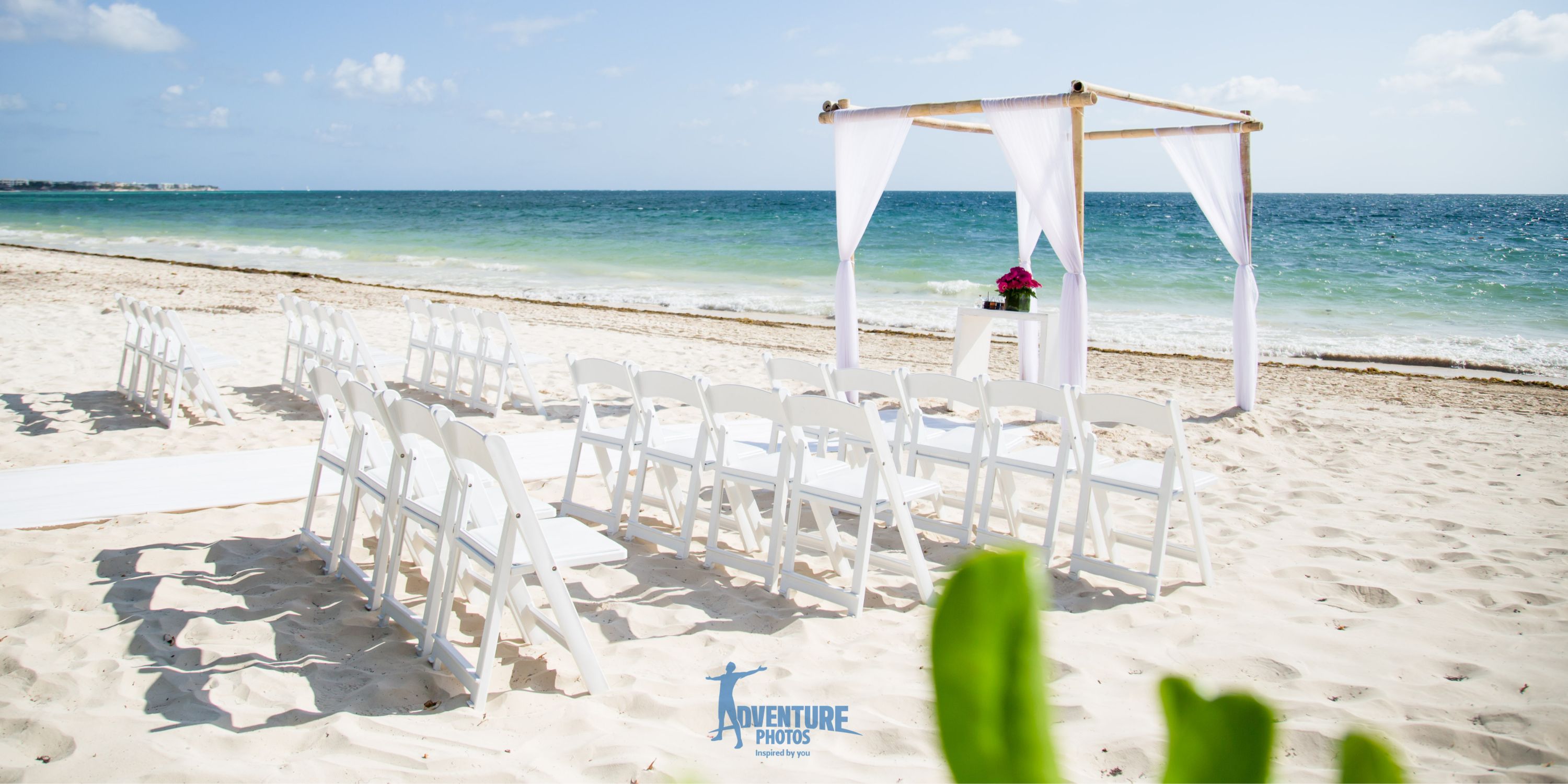 White chairs and a draped altar arranged on the sand for a beautiful destination wedding ceremony.