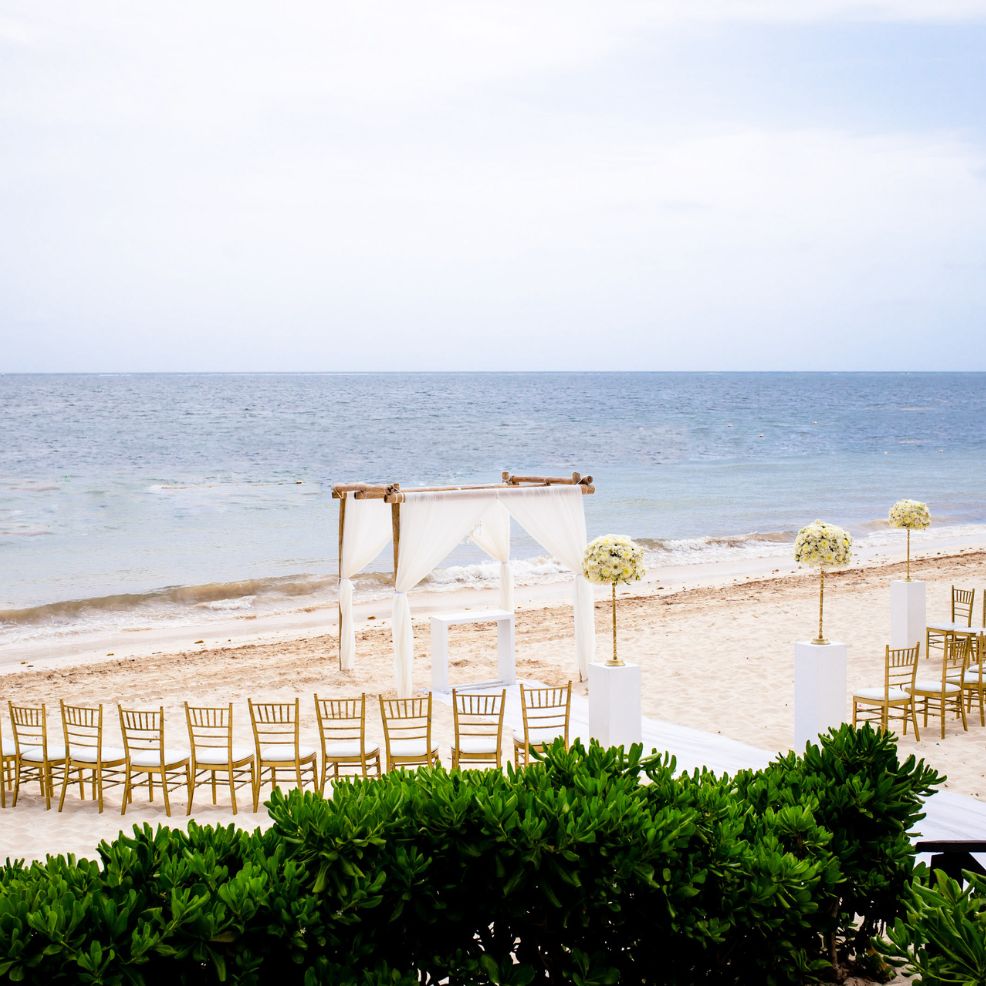 Destination wedding ceremony arrangement with chairs and a canopy on sandy beach overlooking the ocean.