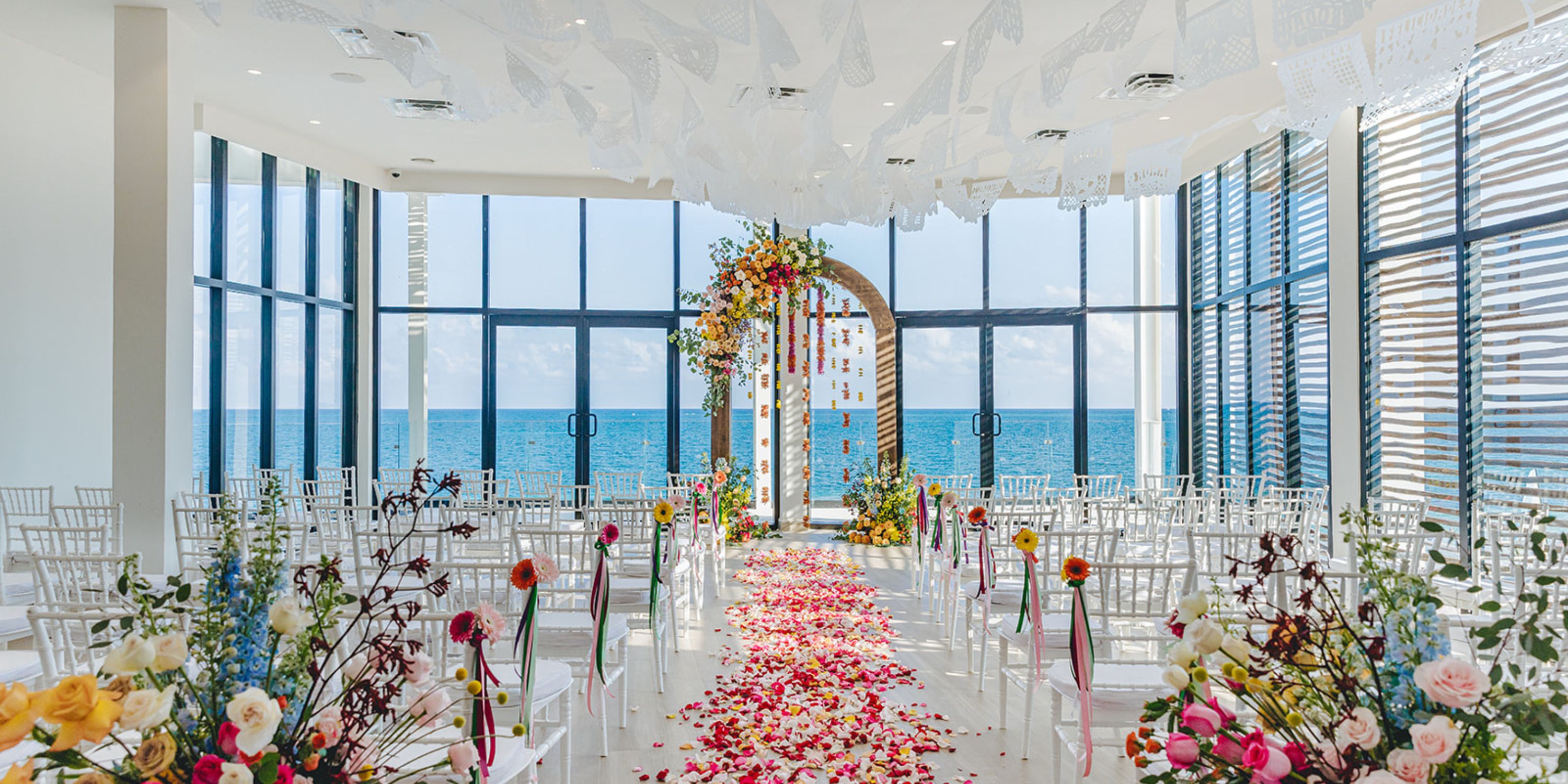 Dreams Sapphire's destination wedding setup showcases floral decor and stunning ocean views through windows.