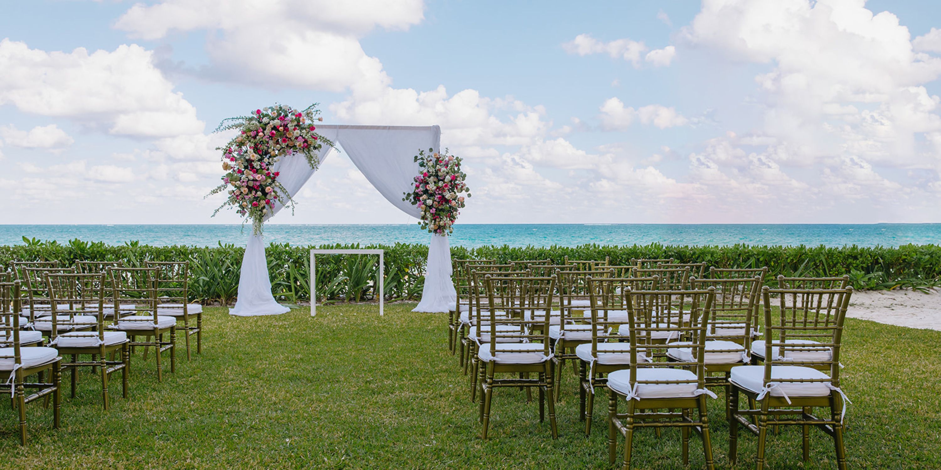 Rows of chairs line up for a destination wedding, facing a floral arch at Dreams Sapphire by the ocean.