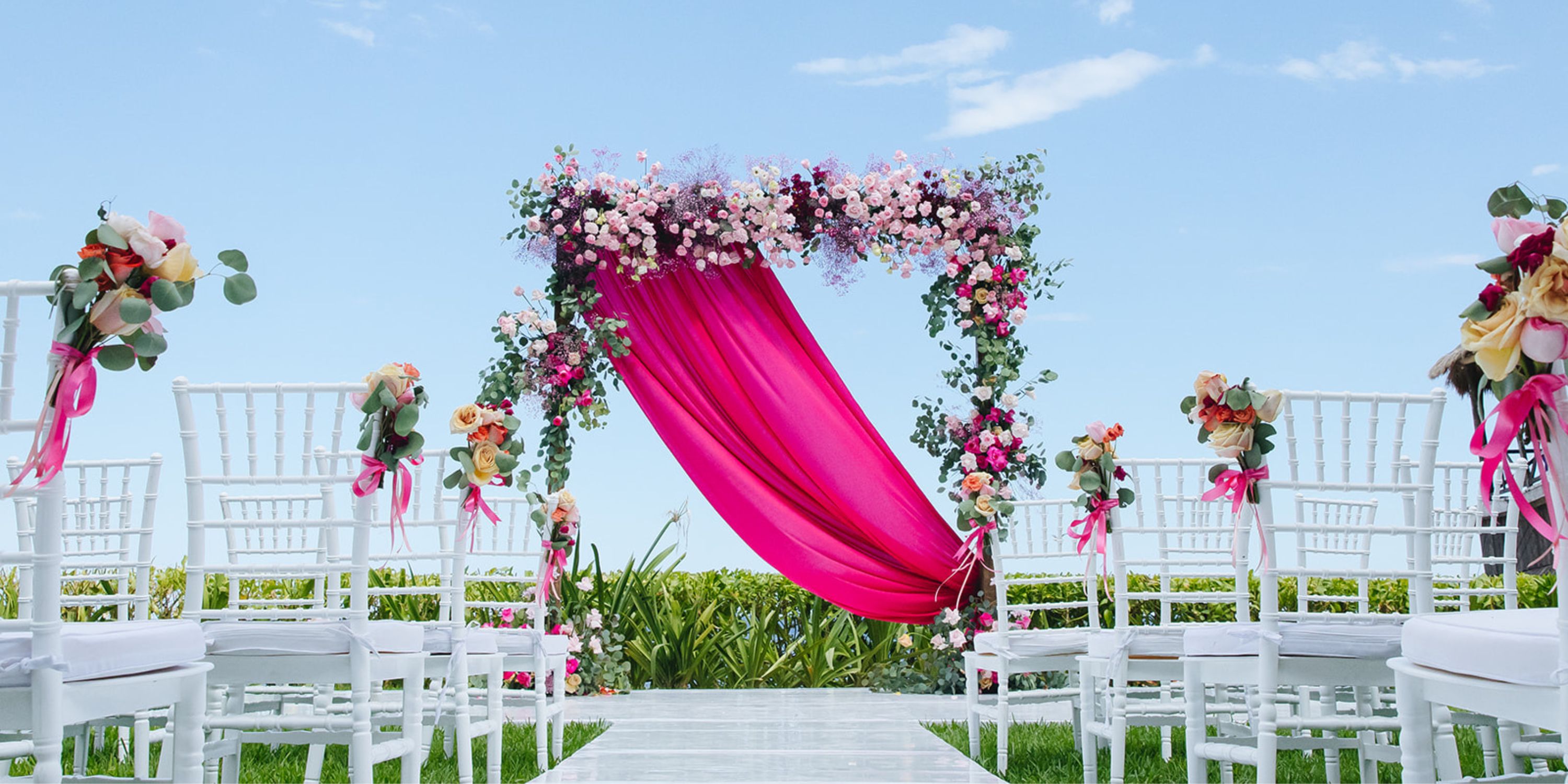 Destination wedding at Dreams Sapphire: white chairs arranged outdoors with a floral arch draped in bright pink.