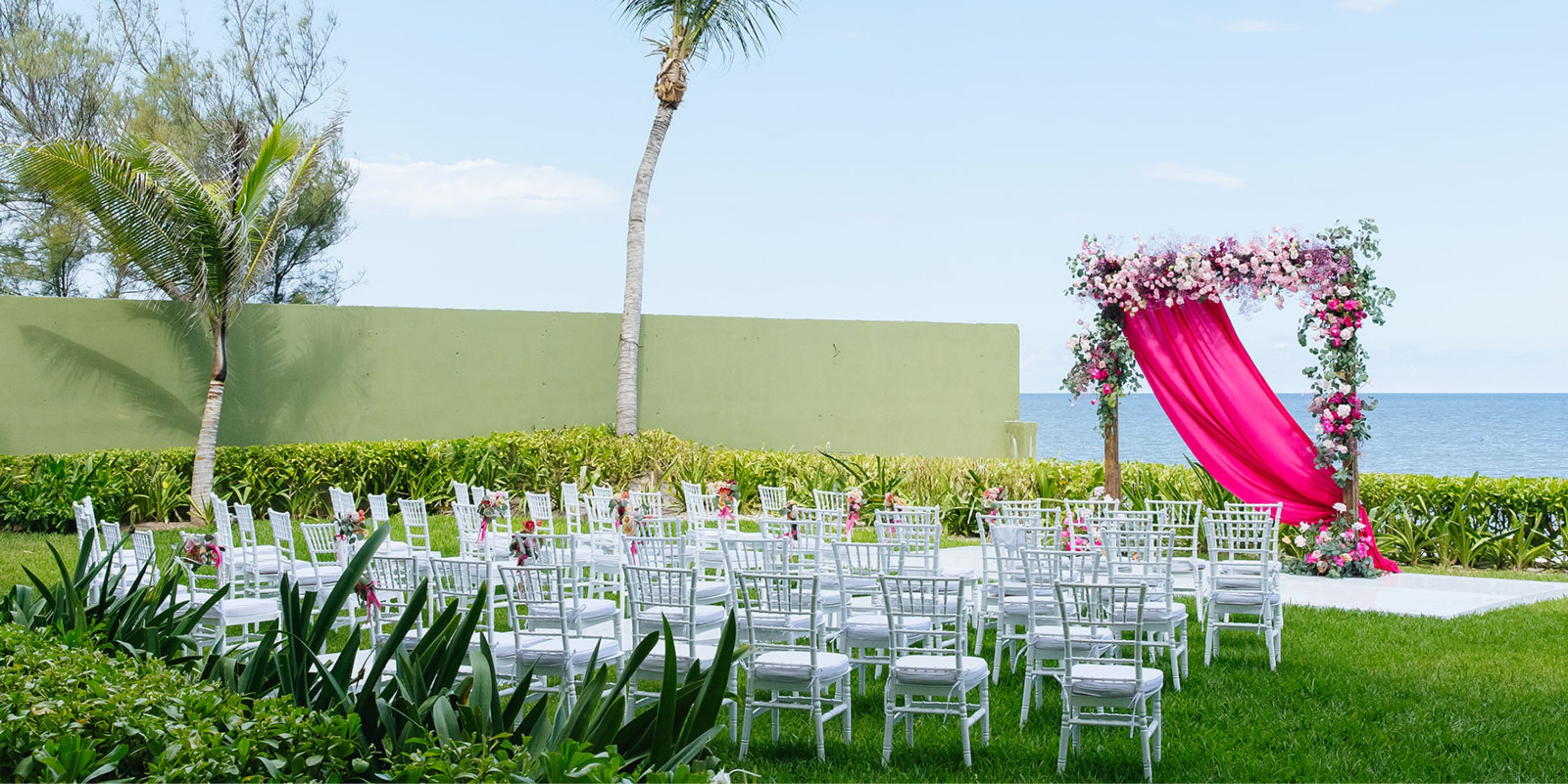 Destination wedding setup at Dreams Sapphire: white chairs face a floral arch overlooking the ocean.