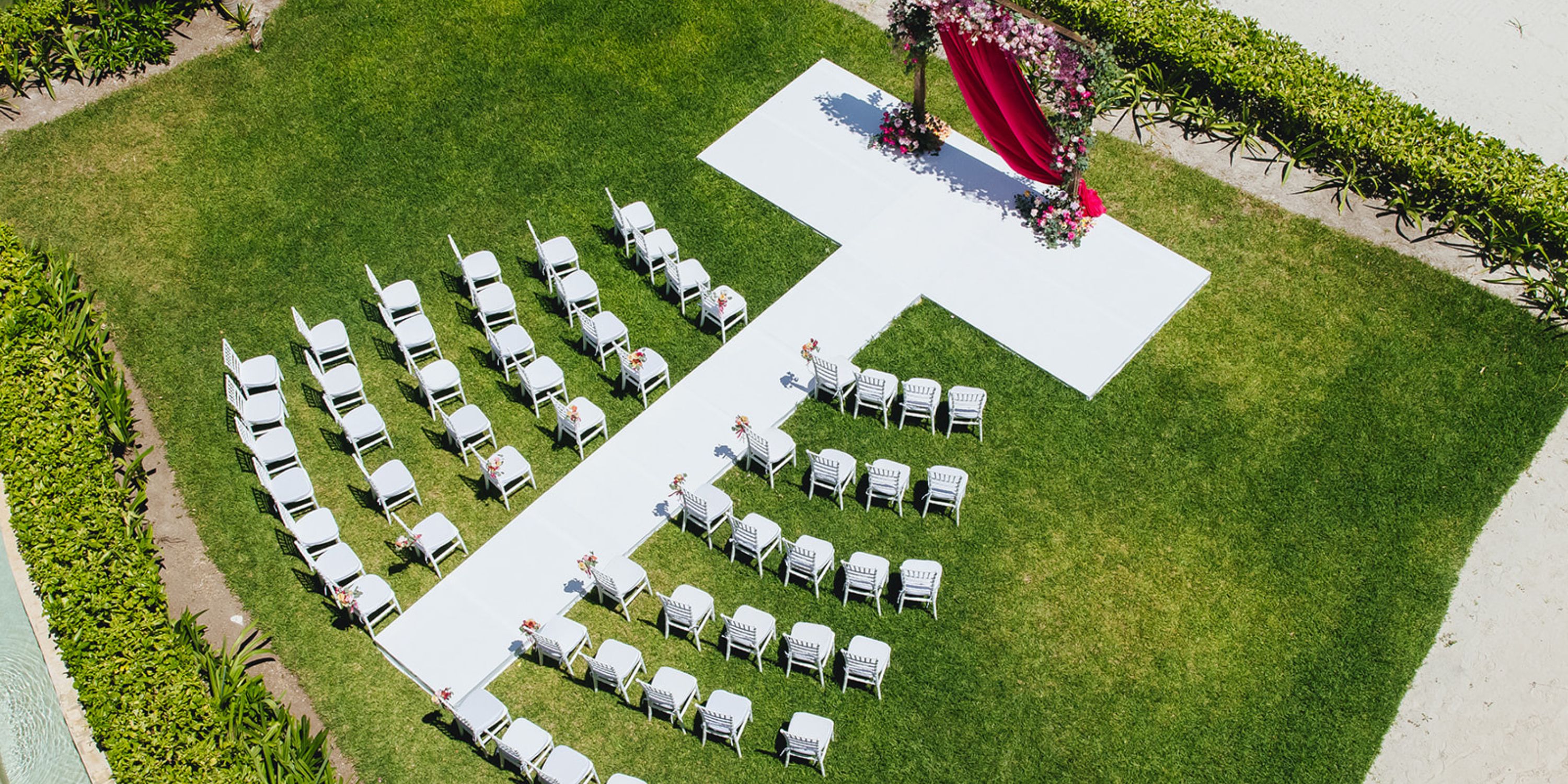 Aerial shot of a destination wedding at Dreams Sapphire, white chairs and a red flower arch on grass.