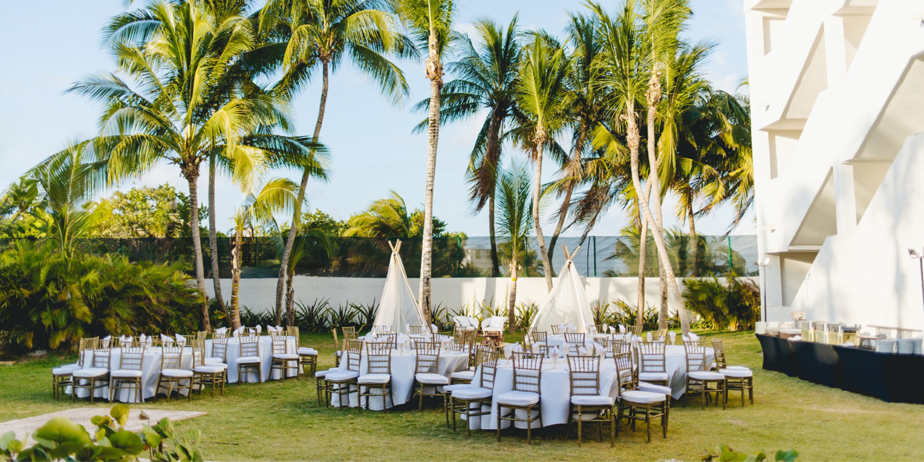 Destination wedding setup at Dreams Sapphire: white chairs, tables, palm trees, and outdoor teepee tents.
