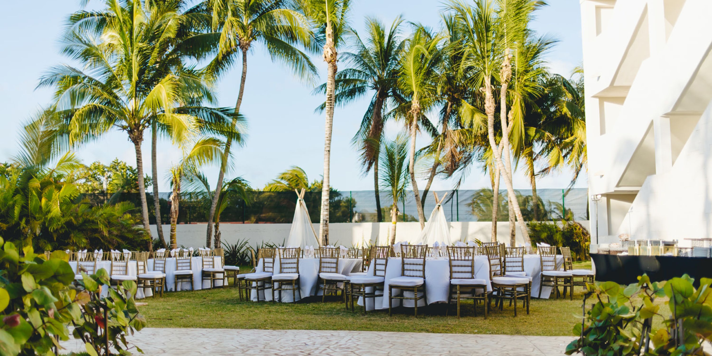Dreams Sapphire destination wedding setup with round tables, chairs, and palm trees on the lawn.