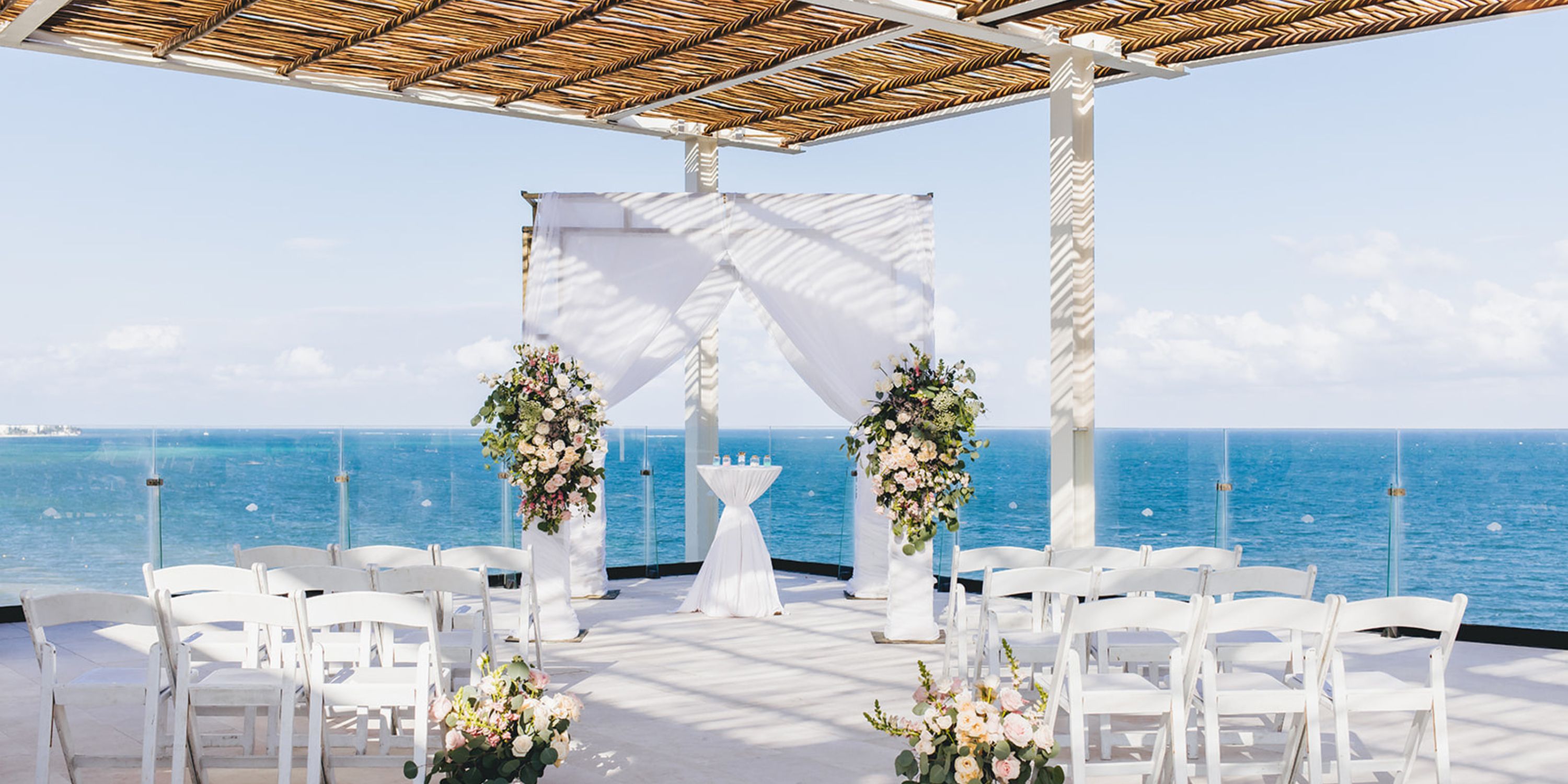 Elegant destination wedding altar at Dreams Sapphire, featuring white chairs, florals, and an ocean view.