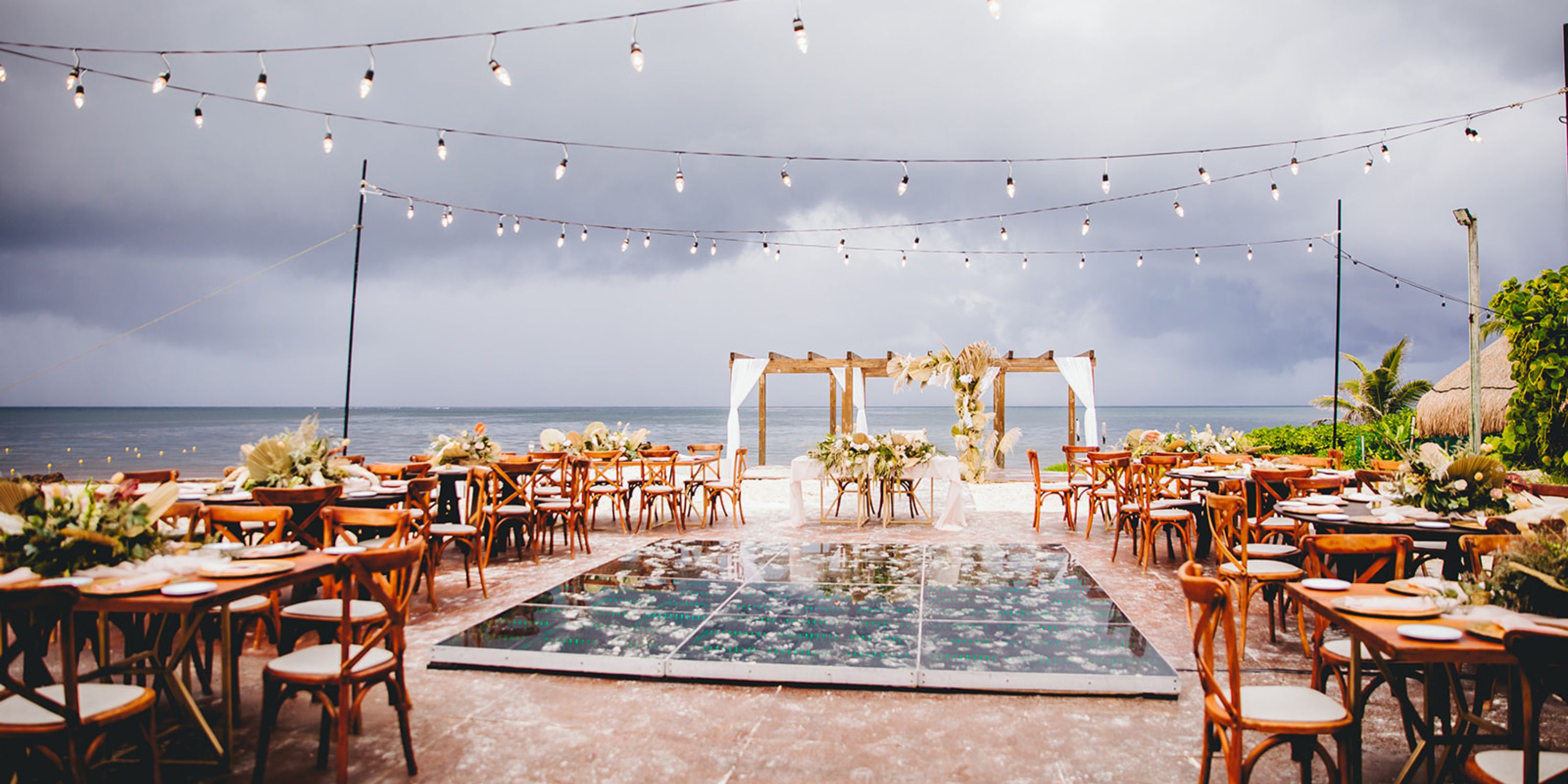 Destination wedding by the ocean at Dreams Sapphire with wooden chairs, an arch, and glowing string lights.