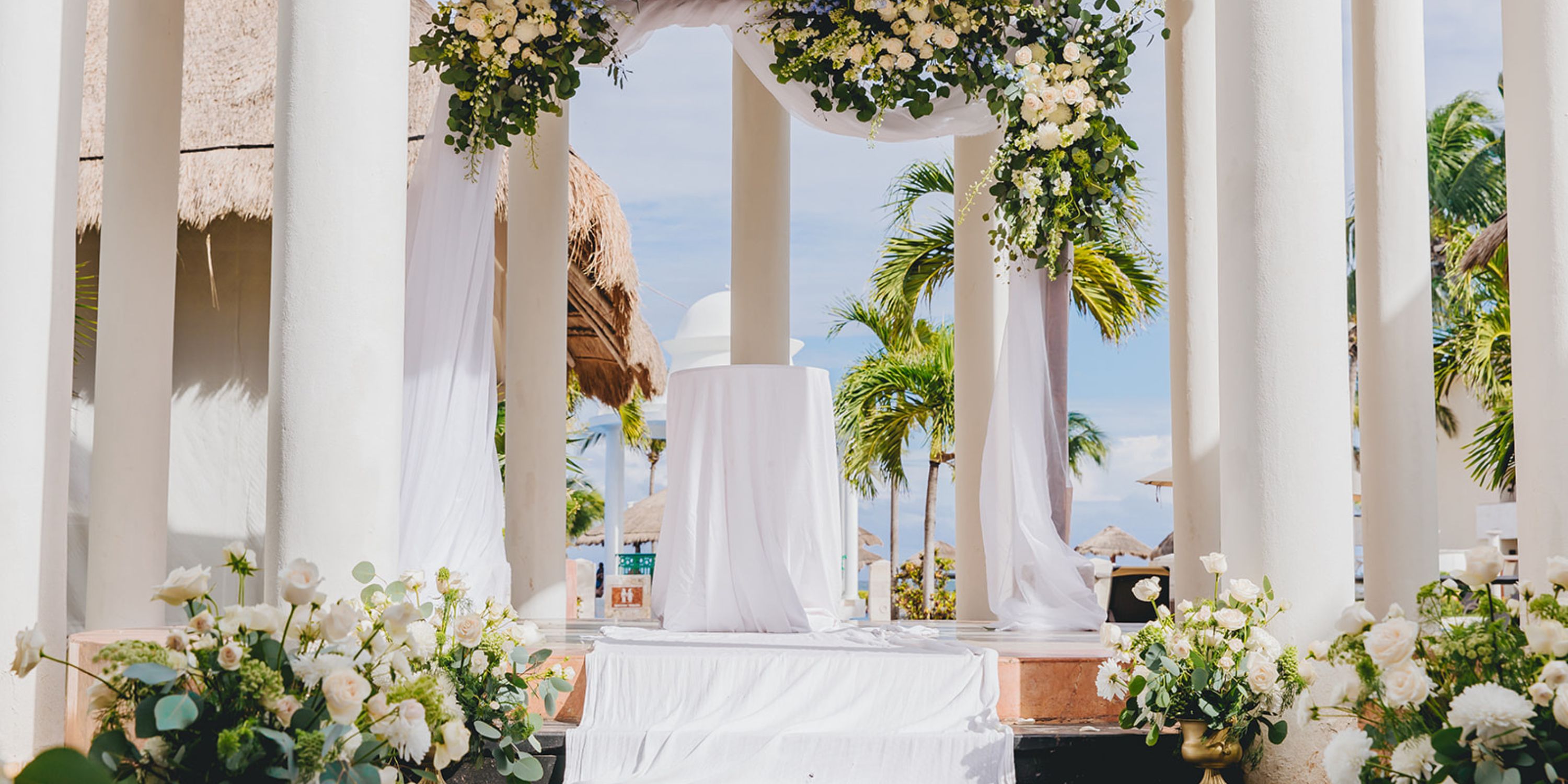 Destination wedding altar at Dreams Sapphire with white columns, draped fabric, and floral arrangements.