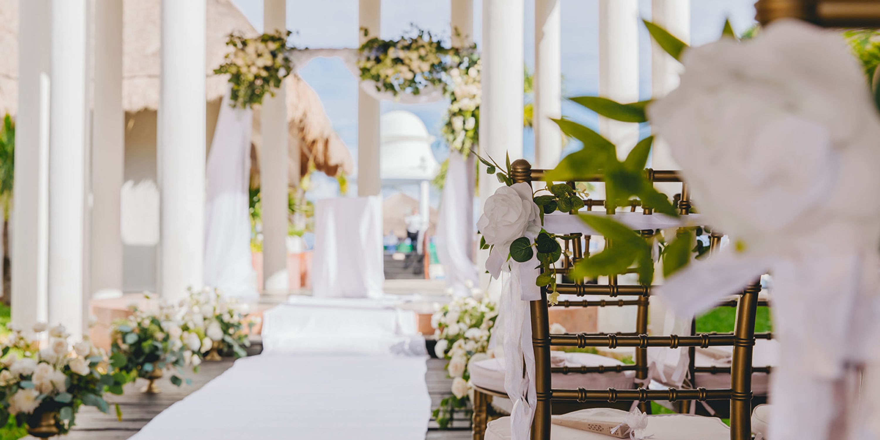 Destination wedding ceremony at Dreams Sapphire featuring white florals, chairs, an arch, and aisle runner.