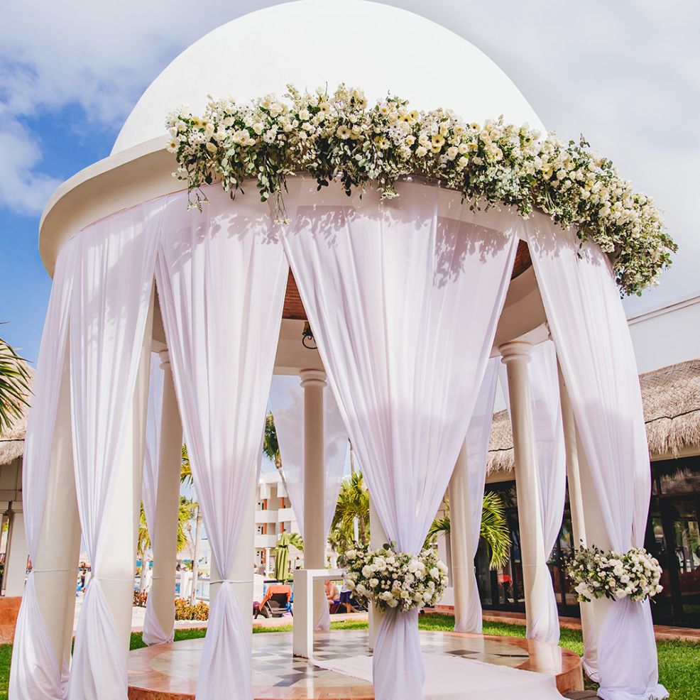 White gazebo adorned with wedding drapery and flowers, perfect for a destination wedding under the clouds.