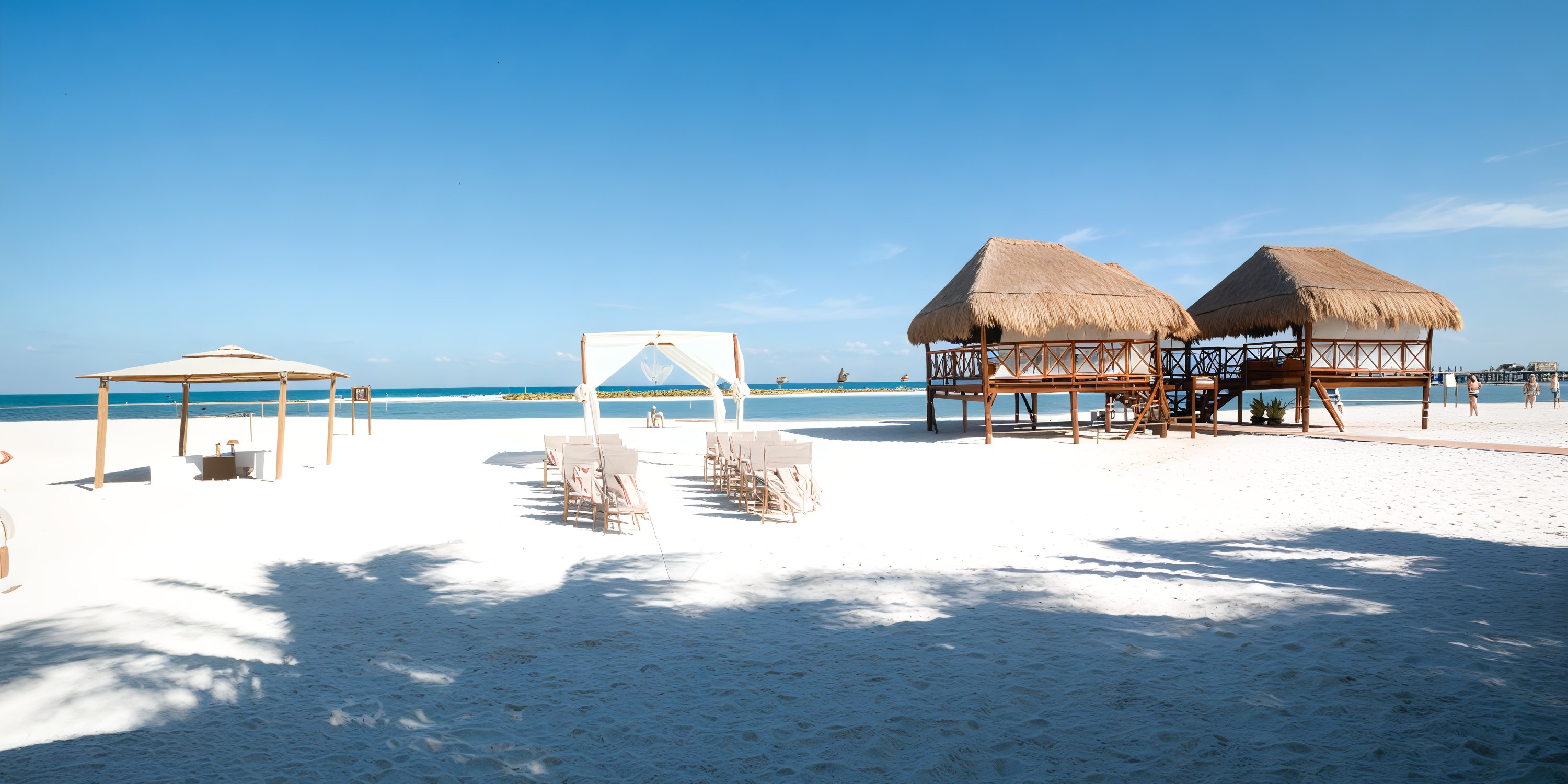 Chairs are elegantly arranged facing a canopy at El Dorado Maroma, making it the perfect setting for a destination wedding, with nearby huts perched on stilts adding to the enchanting atmosphere.
