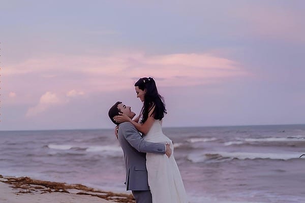 A couple in wedding attire embraces on the beach at sunset during their destination wedding at El Dorado Casitas Royale.
