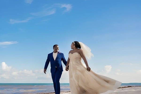 A couple in wedding attire strolls hand-in-hand along the beach at this destination wedding resort.