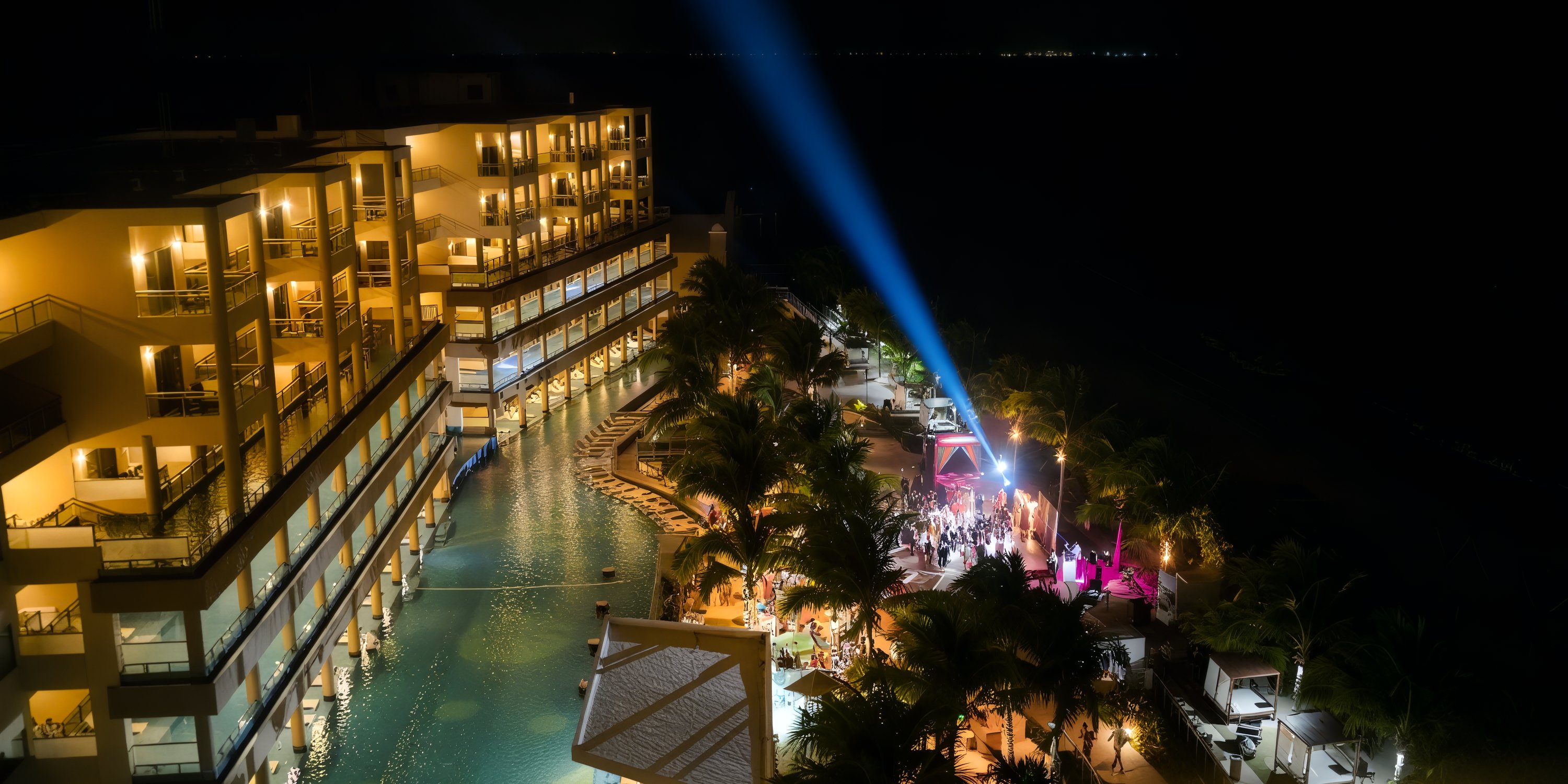 A nighttime scene at Generations Riviera Maya showcases a beautifully illuminated pool surrounded by palm trees and an exquisite event area, perfect for a destination wedding.
